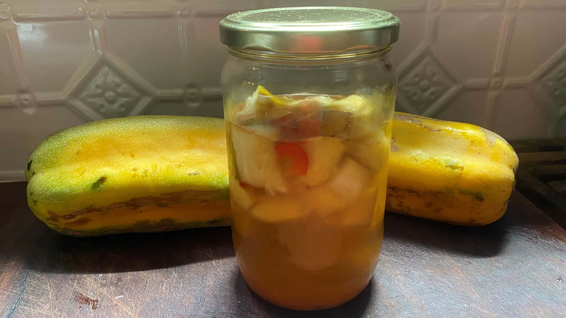 Fruit 桌布 壁紙 — 一個裝滿醃漬木瓜片的玻璃罐放在兩個完整的木瓜之間，置於深色檯面上，背景是瓷磚牆。
