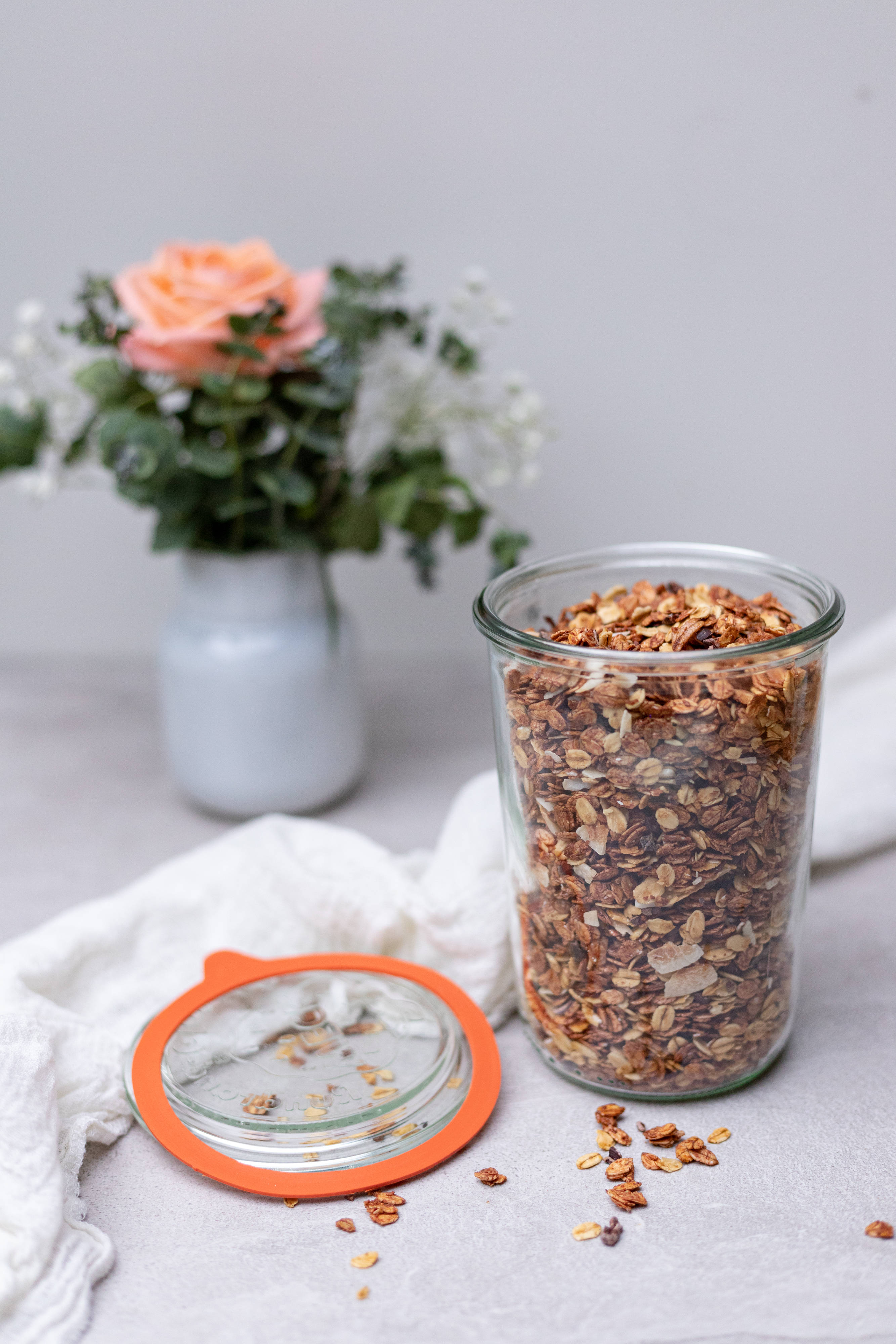 玫瑰花 桌布 壁紙 — 一個裝滿金黃色燕麥片的玻璃罐放在白色布上，旁邊有一個插著蜜桃玫瑰和尤加利葉的花瓶。