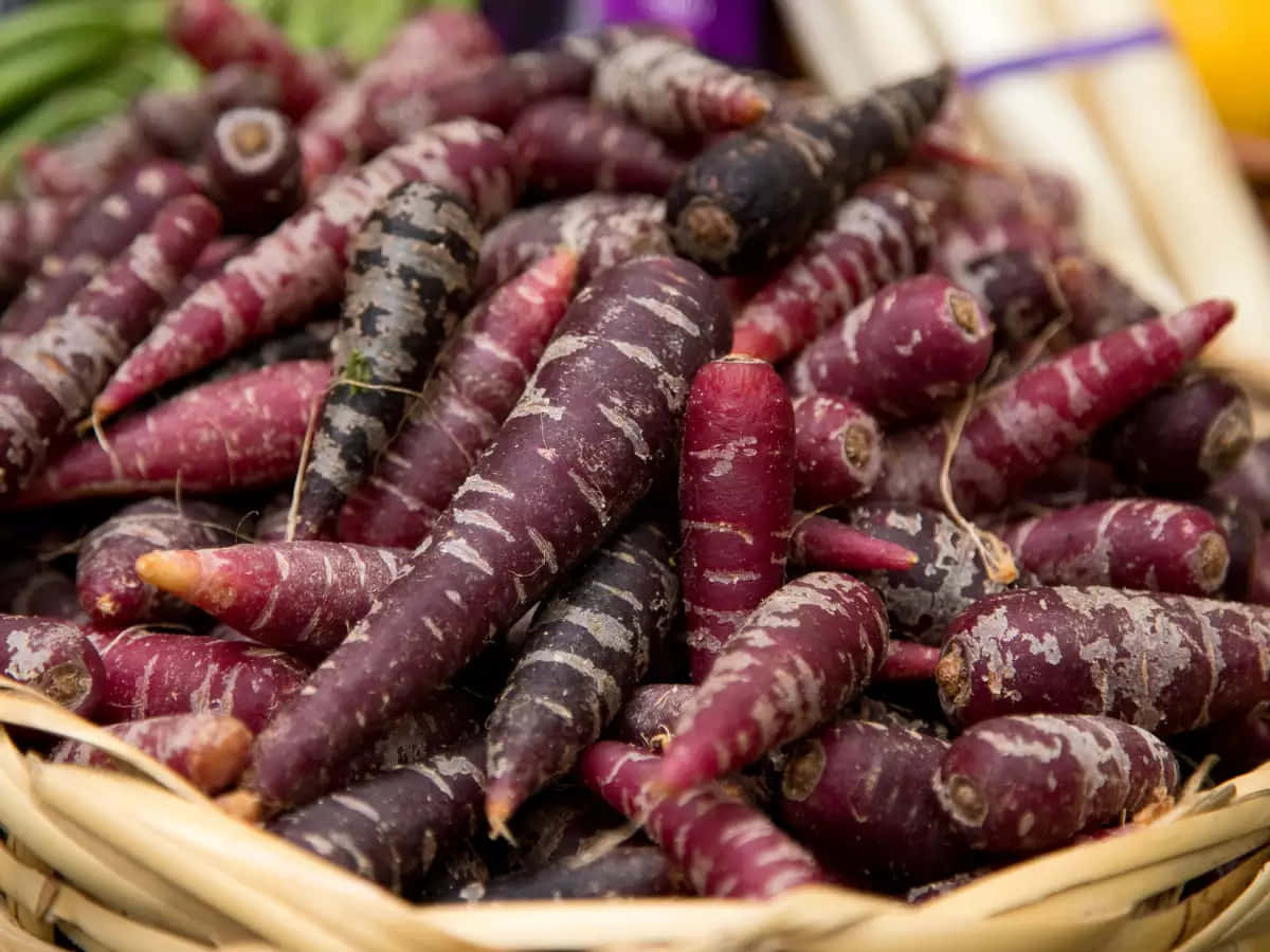 Purple Carrots 桌布 壁紙 — 一個裝滿鮮豔紫色胡蘿蔔的籃子，上面有白色條紋和泥土。