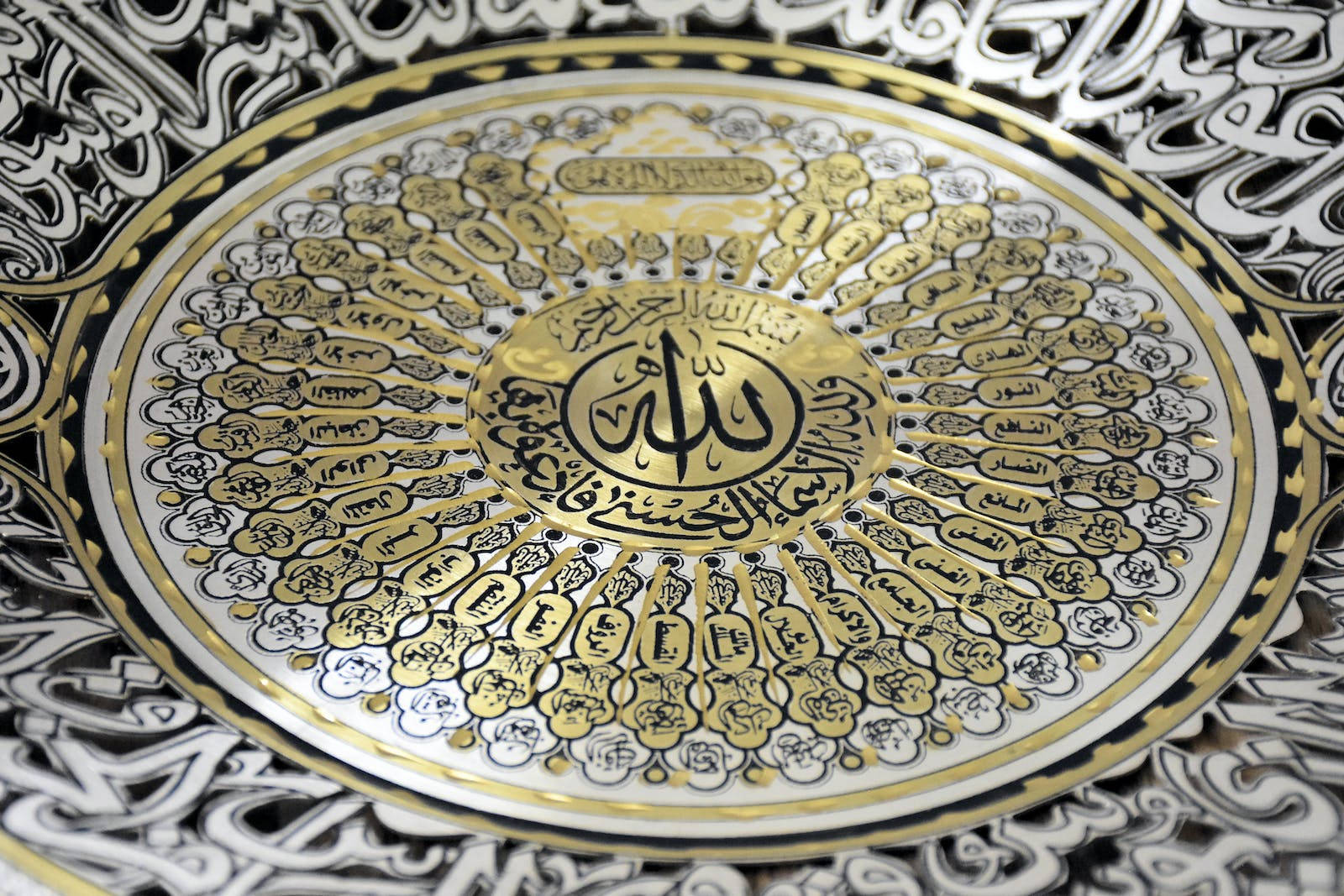 HD Islamic 桌布 壁紙 — 一個裝飾性的圓形盤子上有複雜的金色和黑色阿拉伯書法，從中央神聖的銘文向外輻射。