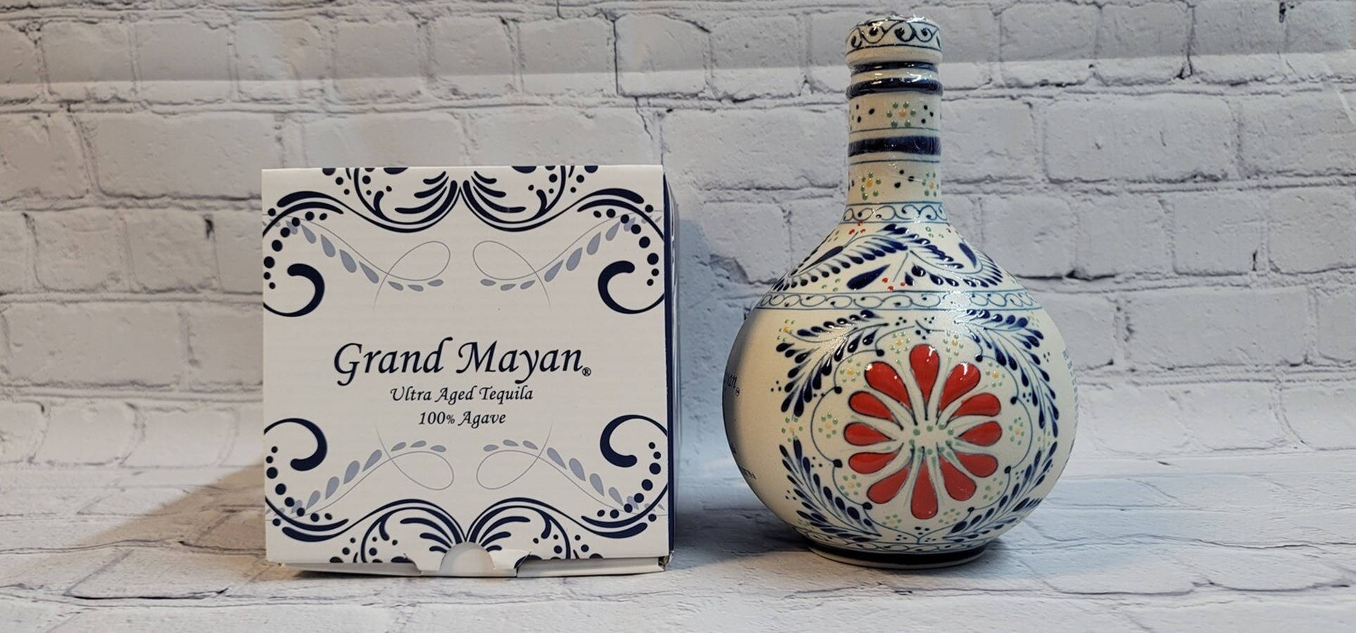 alcohol 桌布 壁紙 — 一個裝飾性的藍紅花卉圖案龍舌蘭酒瓶放在其華麗盒子旁邊，置於白色磚面上。