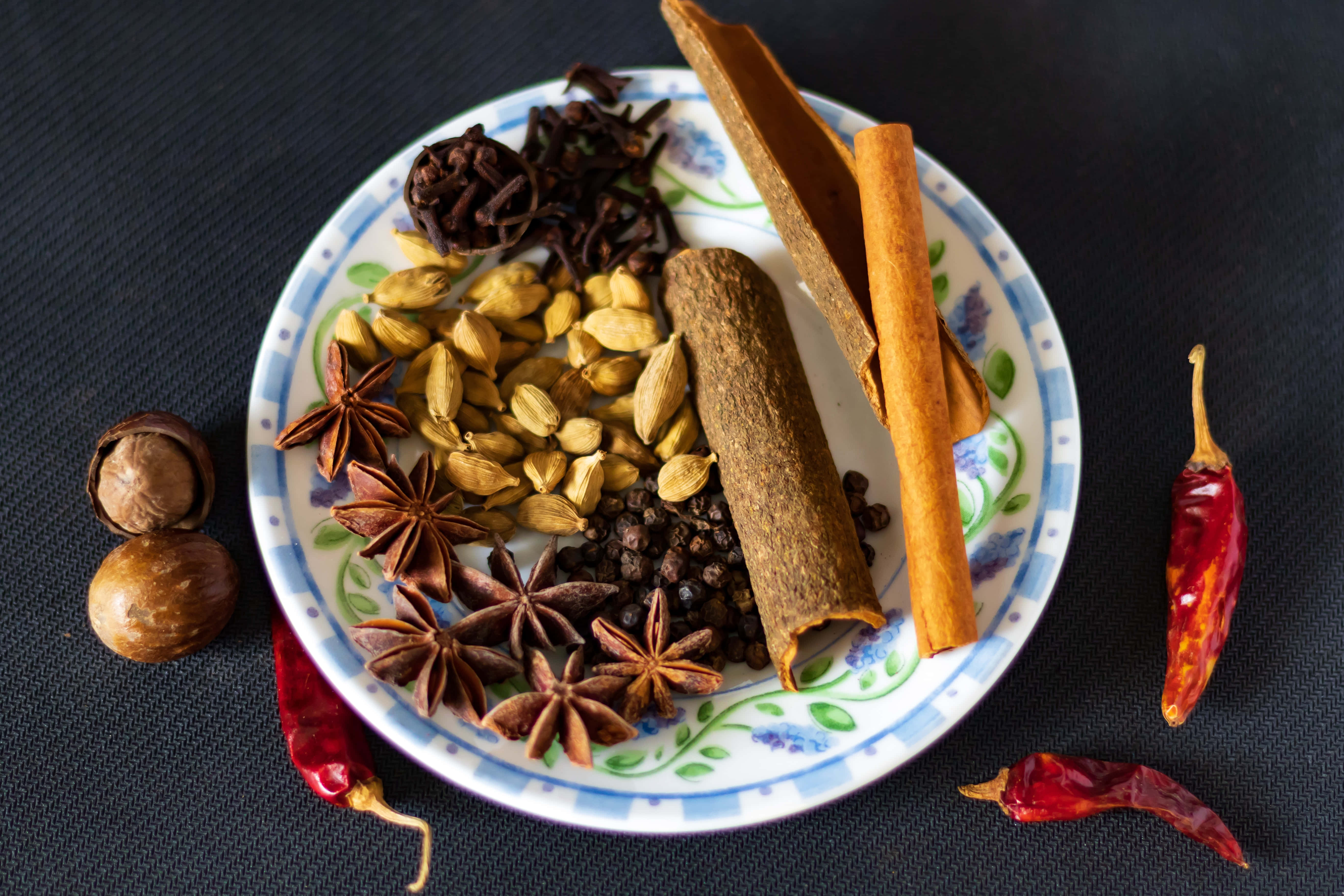 Spices 桌布 壁紙 — 一個裝飾盤盛放著各種原粒香料，包括肉桂棒、荳蔻、八角、丁香，附近散落著乾紅辣椒。