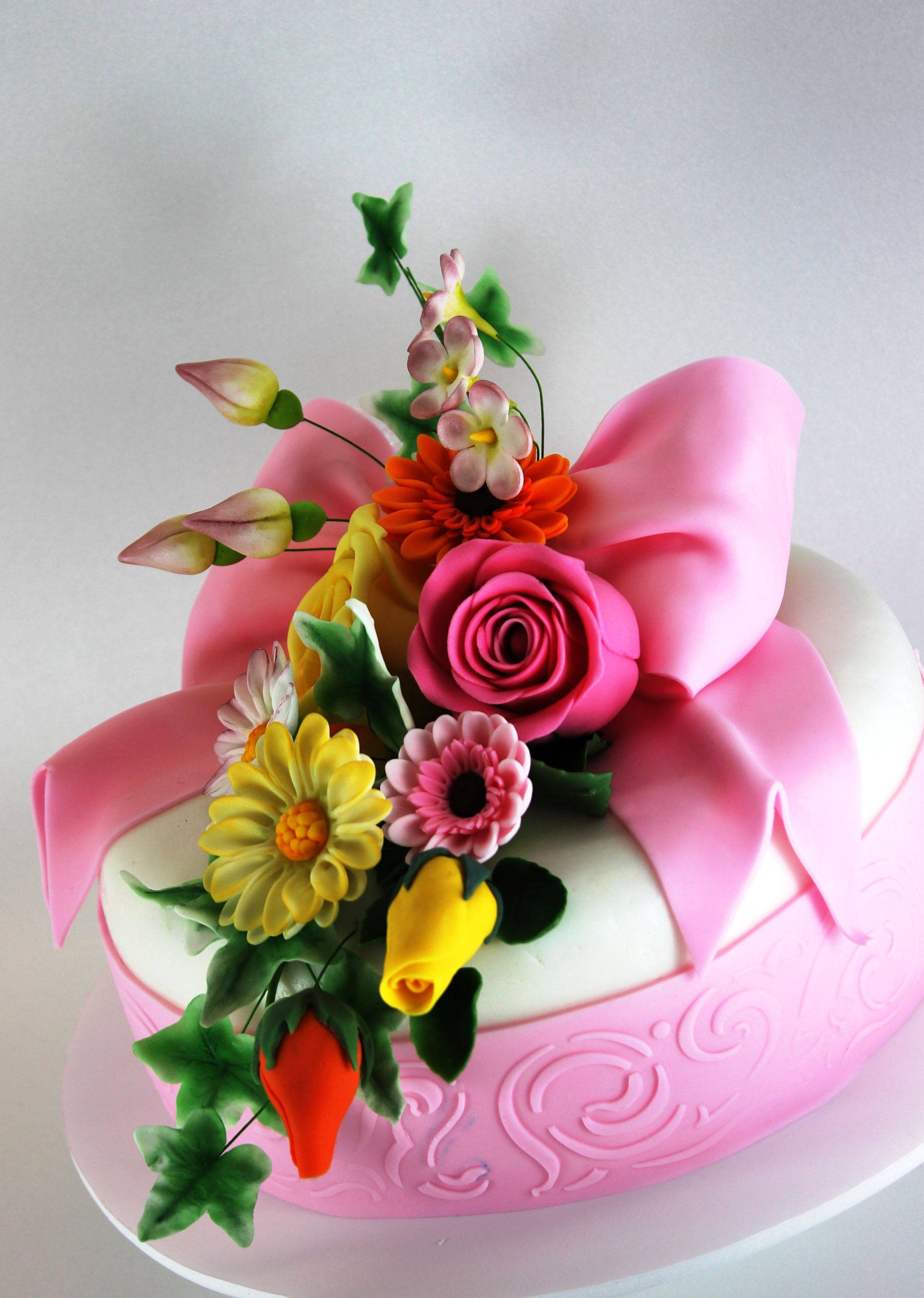Happy Birthday Flower 桌布 壁紙 — 一個裝飾精美的蛋糕，上面有一個大粉紅色蝴蝶結和色彩繽紛的糖花，包括玫瑰、雛菊和鬱金香。