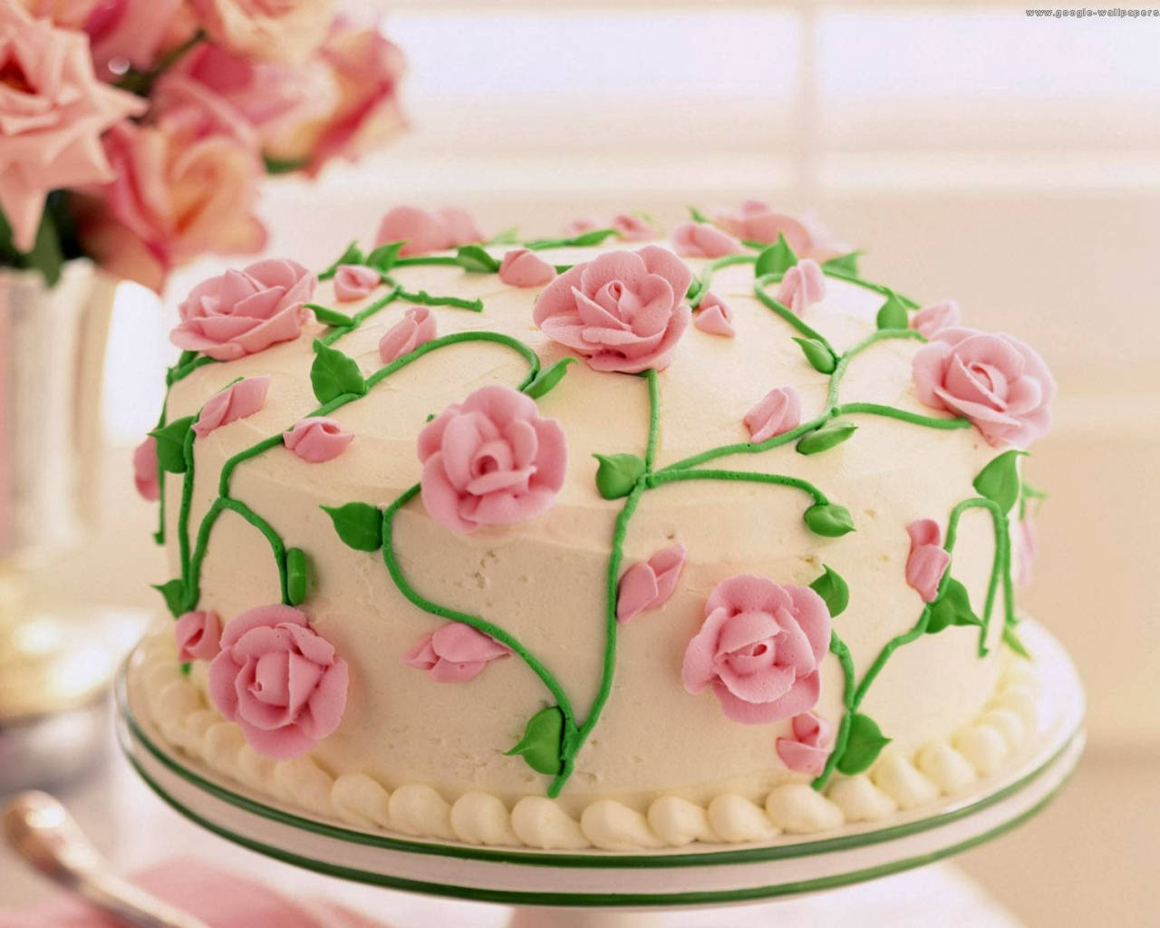 Happy Birthday Flower 桌布 壁紙 — 一個裝飾精美的蛋糕，上面有粉紅玫瑰和綠色藤蔓，放在奶油糖霜上，優雅地立在底座上。