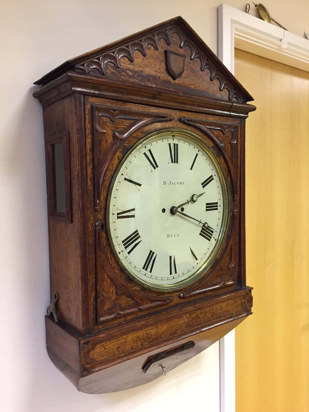 Wall Clock 桌布 壁紙 — 一個裝飾華麗的古董木製掛鐘，帶有羅馬數字，掛在門旁邊的素牆上。