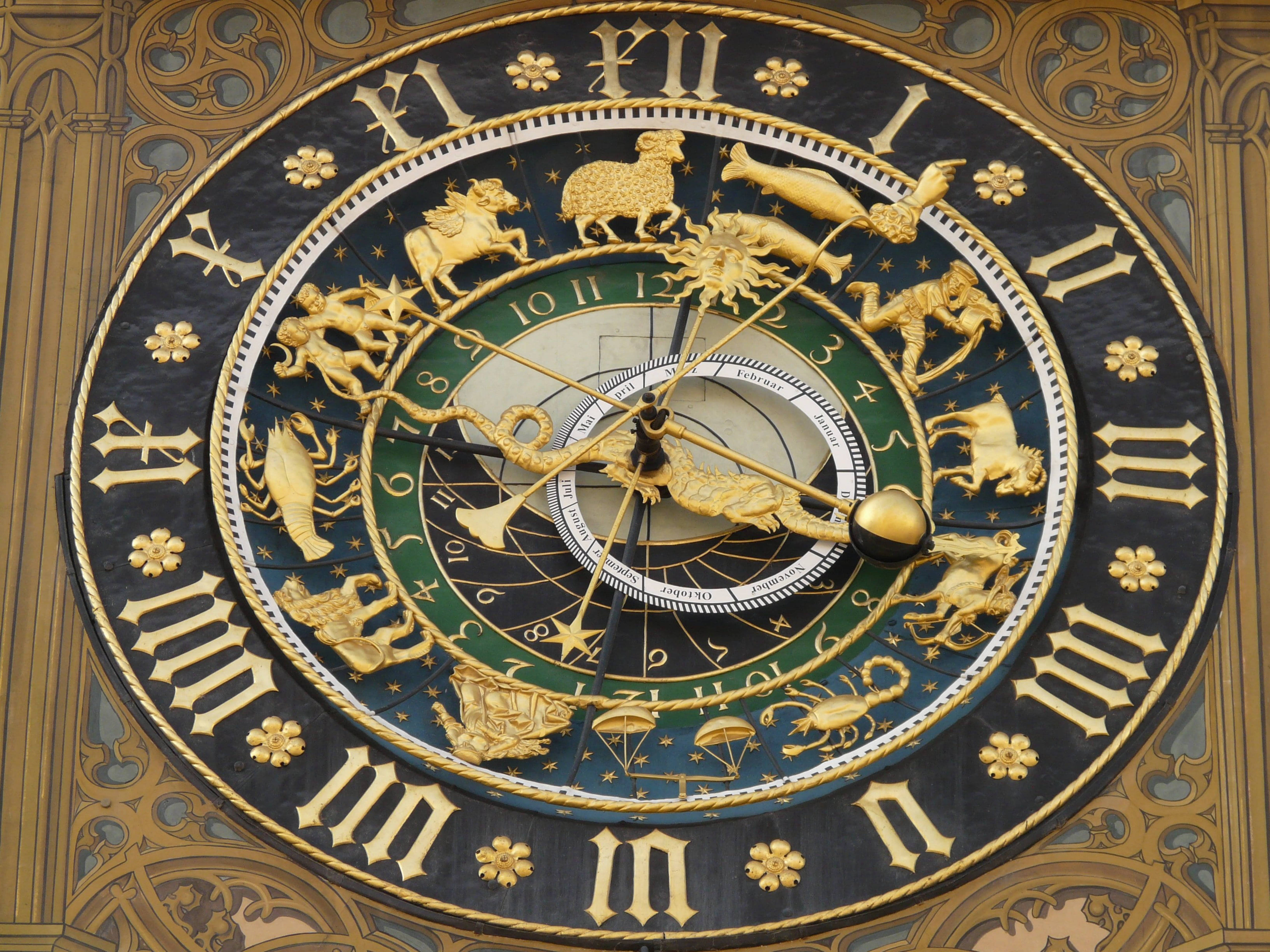 zodiac 桌布 壁紙 — 一個裝飾華麗的金色天文鐘，帶有星座符號和羅馬數字，背景為深藍色。