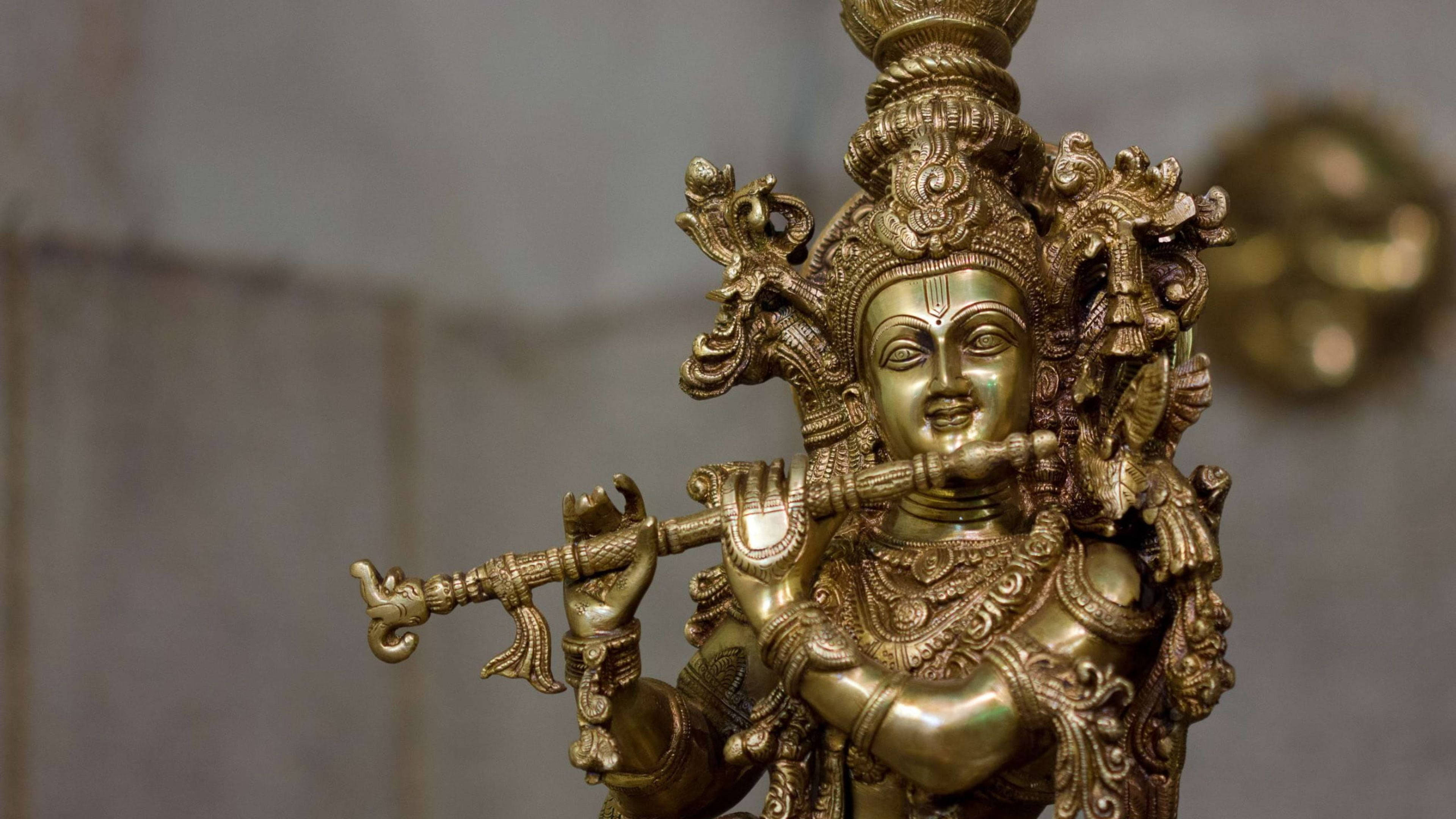 krishna ji 桌布 壁紙 — 一個裝飾華麗的金色神像吹奏長笛的特寫，雕刻精細，表情寧靜。