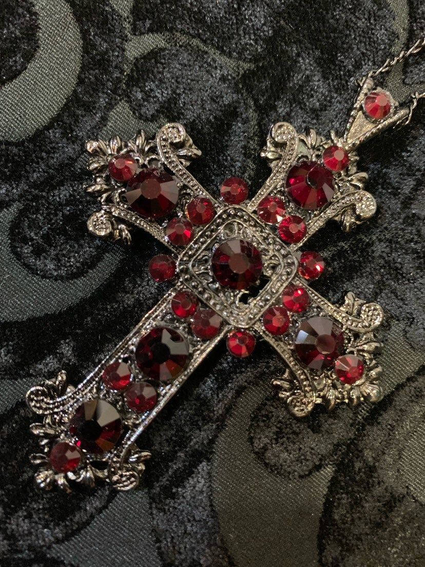 Red Crystal 桌布 壁紙 — 一個裝飾華麗的銀色十字架，鑲嵌著深紅色寶石，放置在深色圖案布料上。