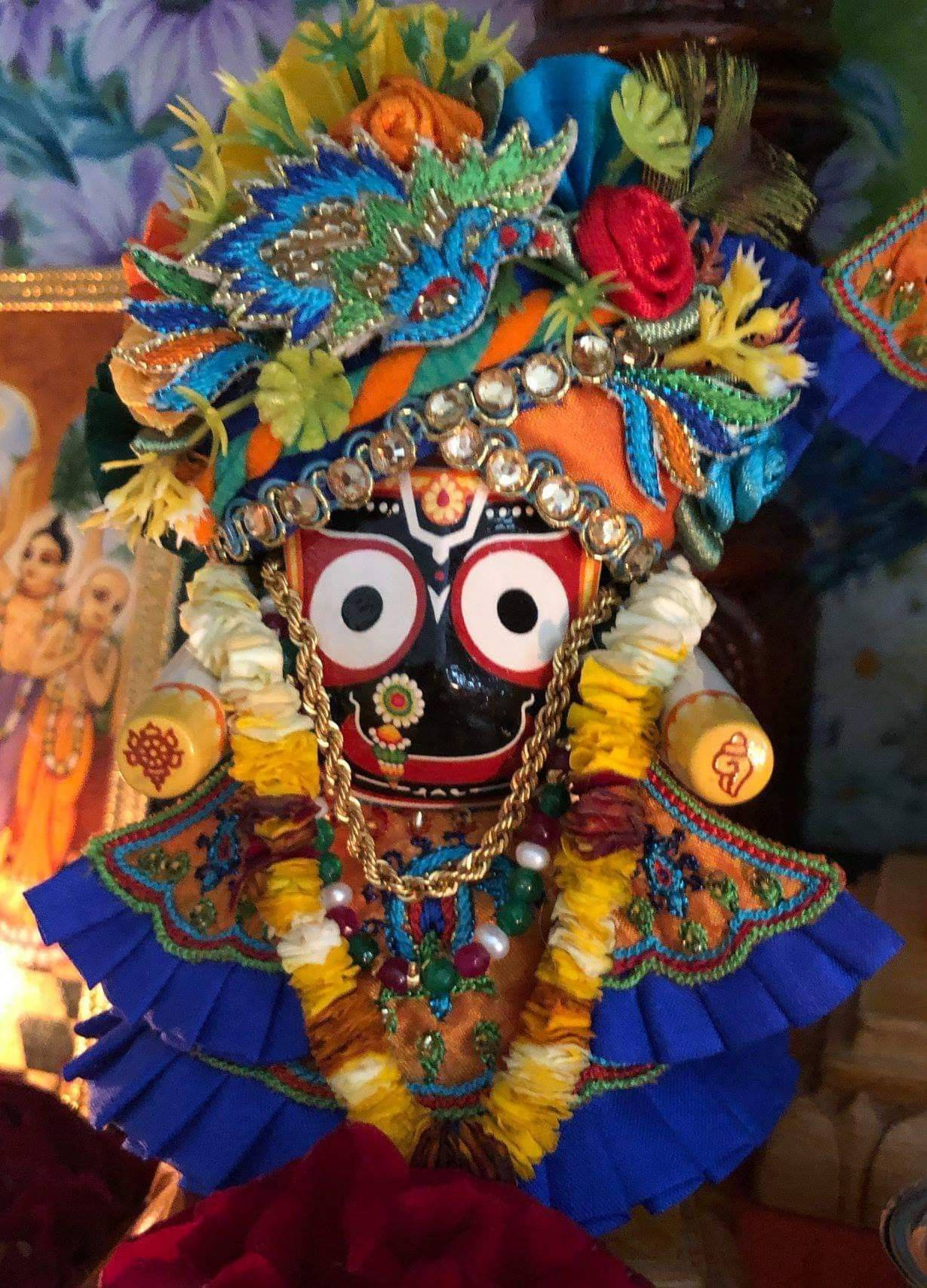 Jagannath 桌布 壁紙 — 一個裝飾鮮豔的印度教神像，飾有彩色花珠和華麗珠寶，背景為圖案背景。