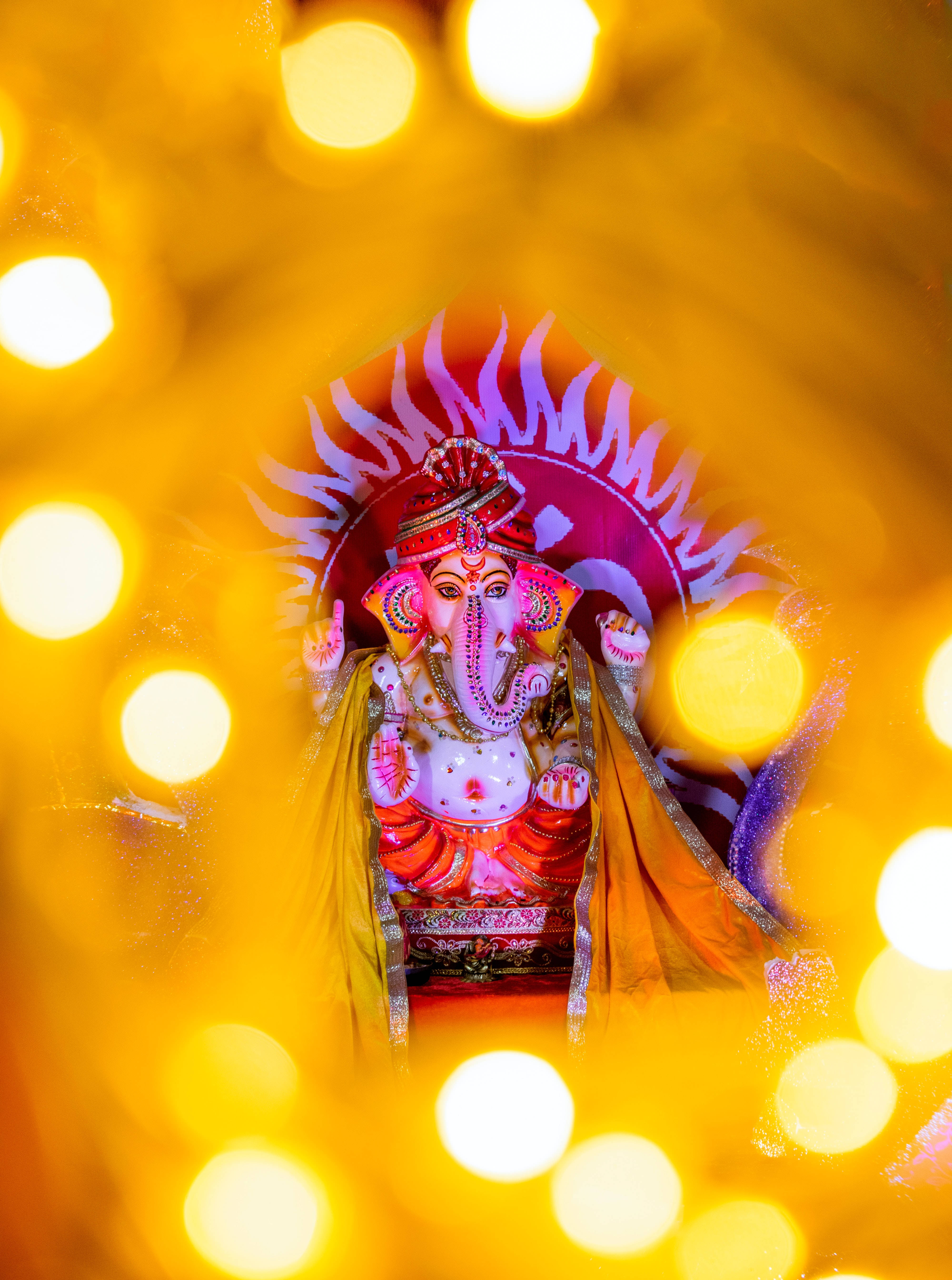 Ganesh 桌布 壁紙 — 一個裝飾鮮豔的象神像莊嚴地坐在閃爍的金色散景燈光中。