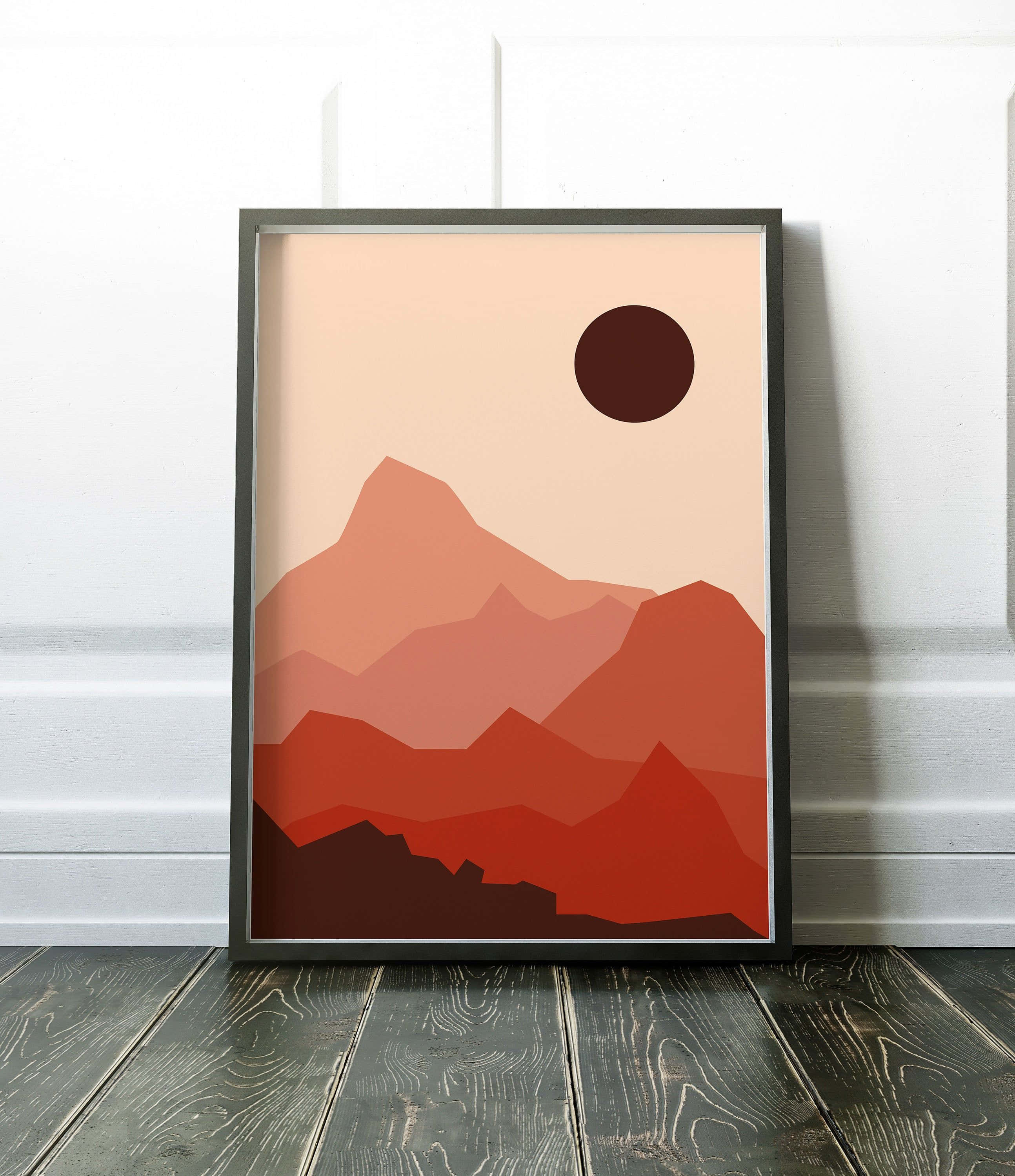 Modern Minimalist Art 桌布 壁紙 — 一個裱框的極簡主義山脈藝術印刷品，帶有層疊的陶土色山峰和一個深色太陽，襯著蜜桃色天空，靠在一面白牆上，地板是深色木地板。