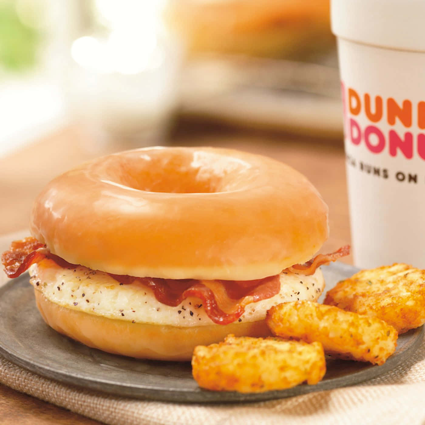 Glazed Donut 桌布 壁紙 — 一個裹著糖霜的甜甜圈三明治，夾著培根和雞蛋，放在一個有薯球和Dunkin' Donuts杯的盤子上。