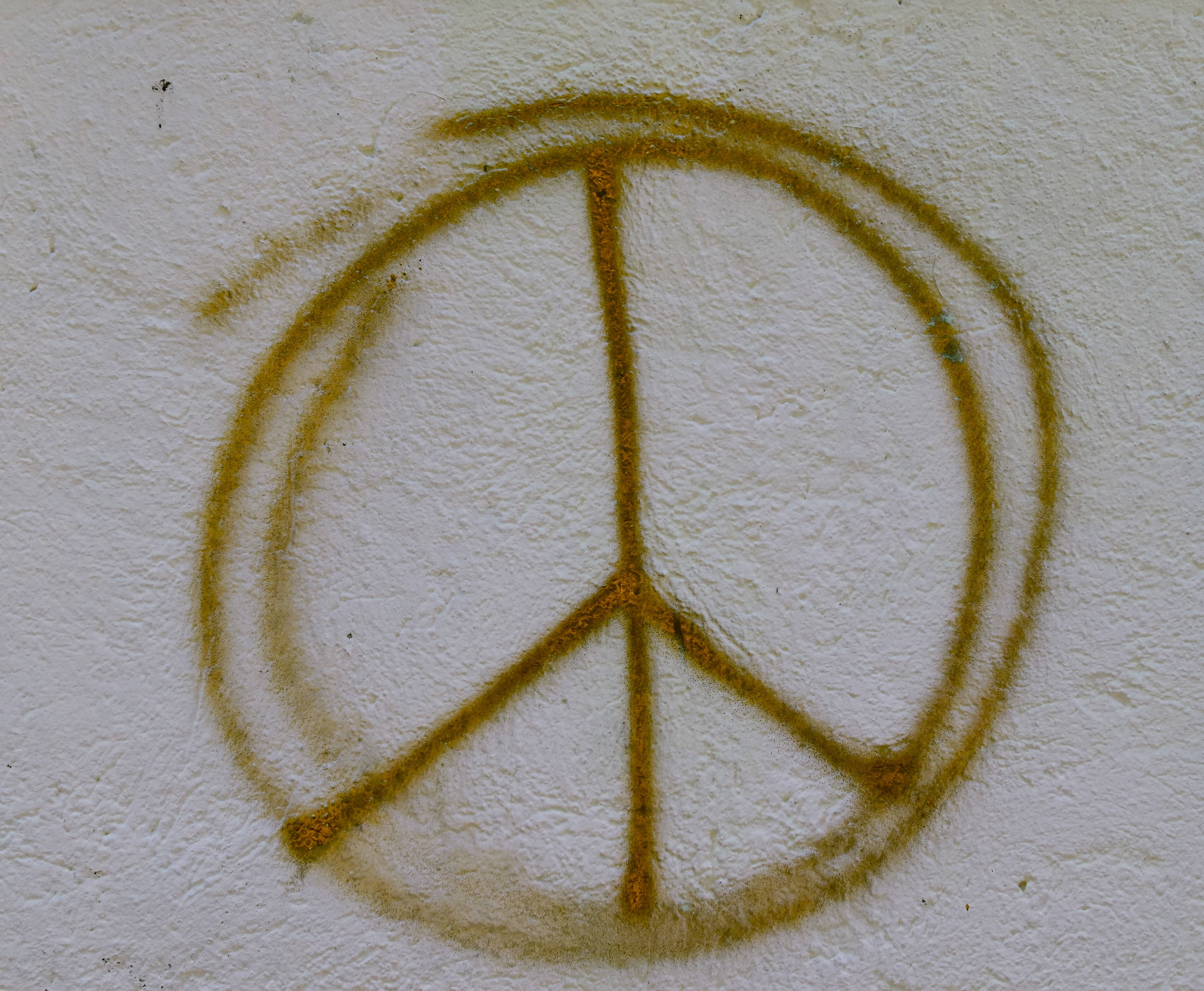 Peace Symbol 桌布 壁紙 — 一個褪色的橙色和平符號噴在粗糙的白色灰泥牆上，帶有可見的紋理和磨損。