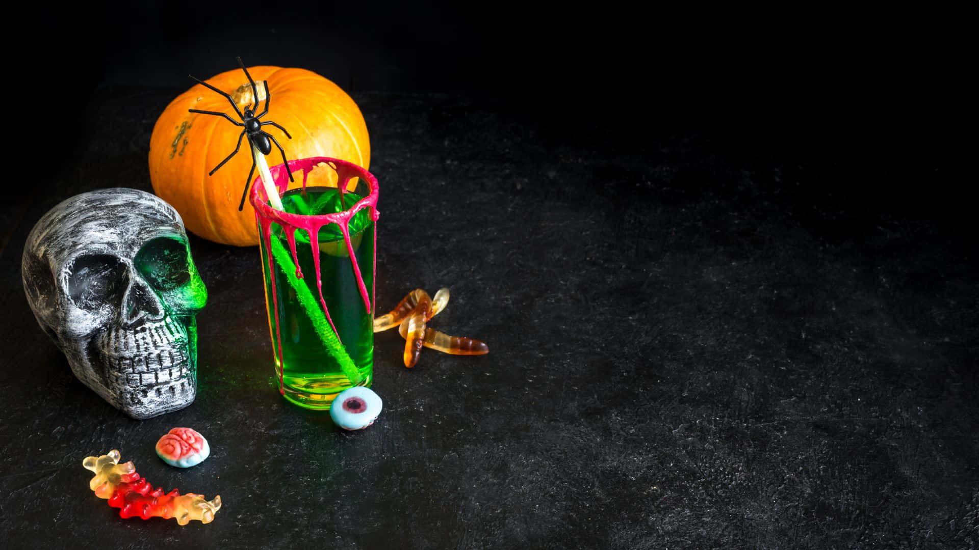 Spooky Cocktails 桌布 壁紙 — 一個詭異的萬聖節靜物，包括頭骨、南瓜、蜘蛛和綠色飲料，放置在深色紋理表面上。