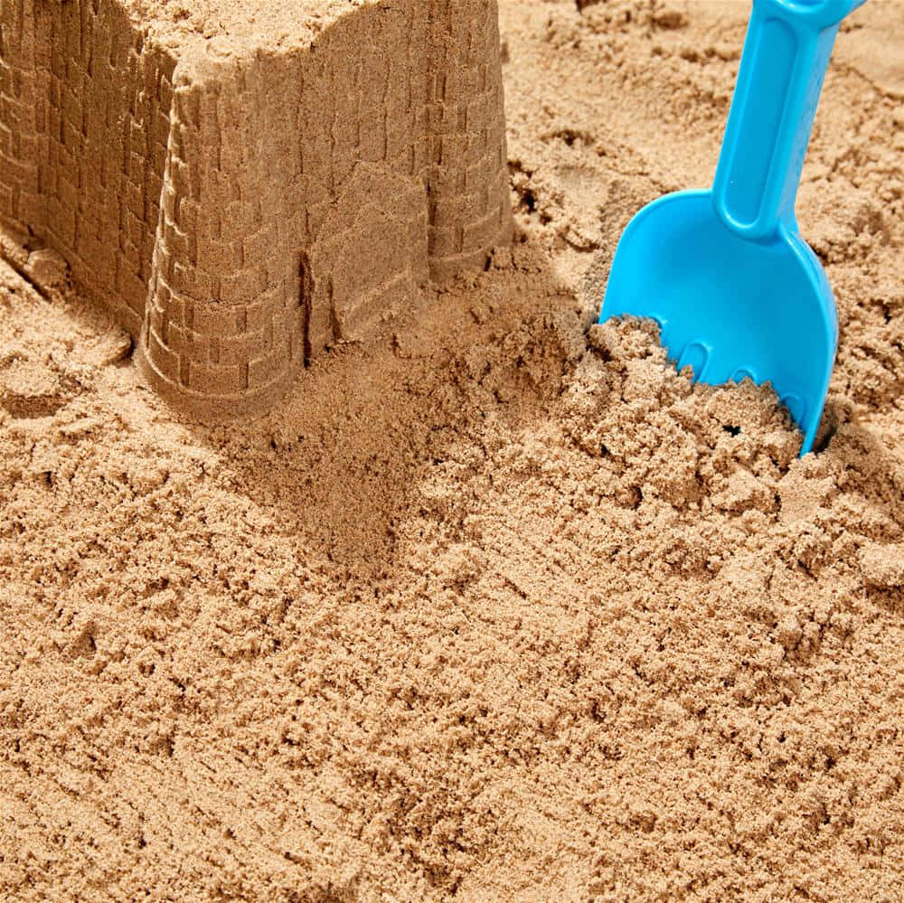 sand 桌布 壁紙 — 一個詳細沙堡塔的特寫，旁邊有一個亮藍色塑料鏟子放在有紋理的沙子上。