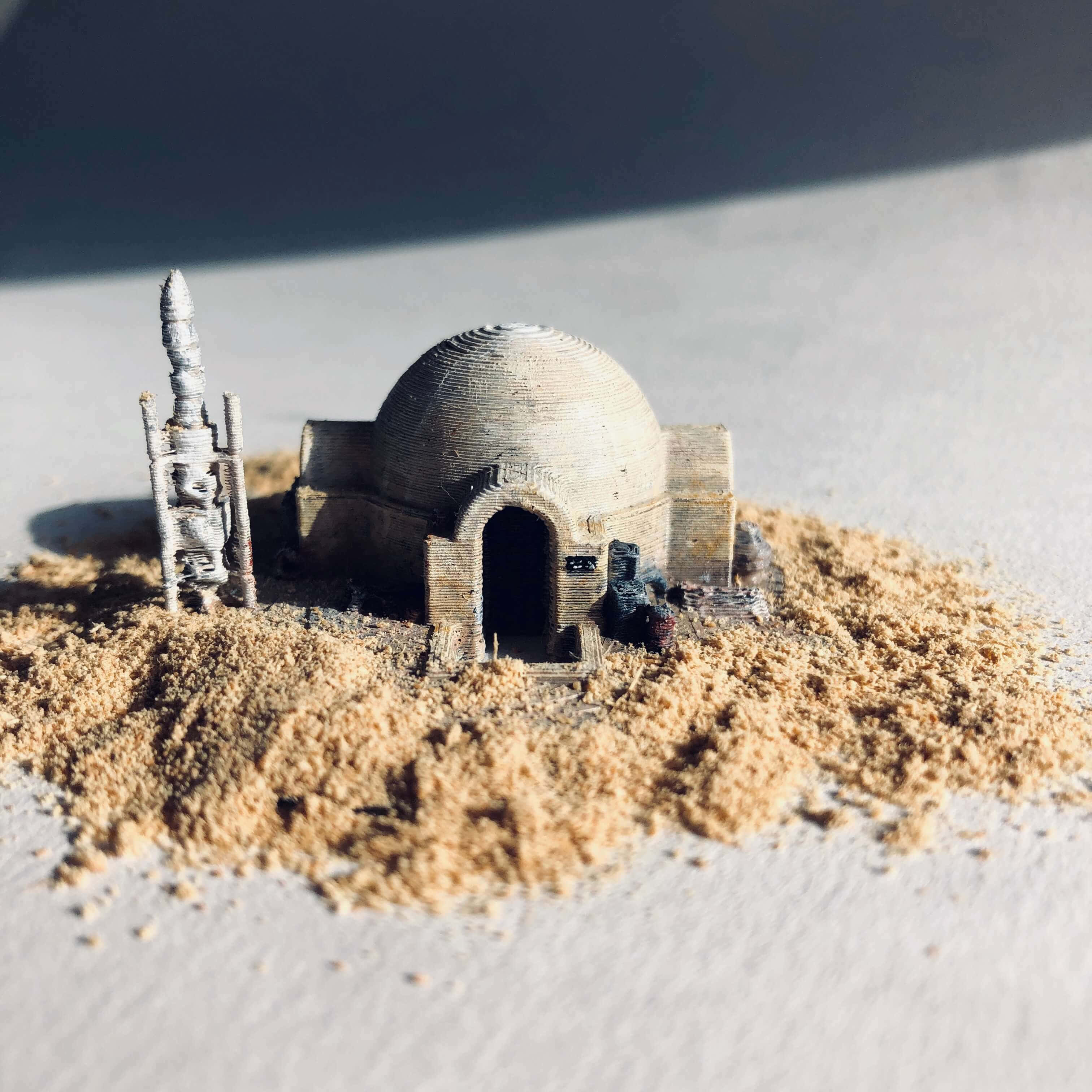 Tatooine 桌布 壁紙 — 一個詳細的3D列印沙漠圓頂房屋模型，帶有高塔，坐落在沙堆上，處於明亮的陽光下。