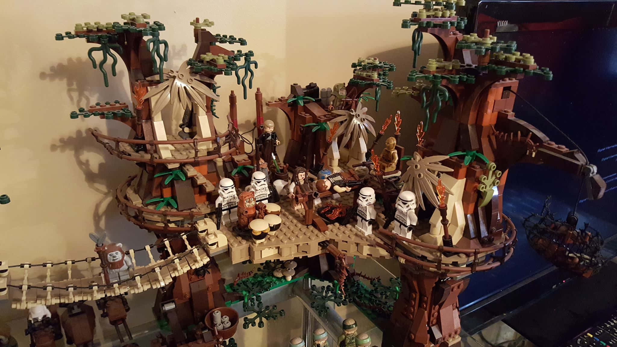 Ewok Village 桌布 壁紙 — 一個詳細的LEGO Star Wars樹屋村莊，有風暴兵和伊渥克人聚集在篝火旁，上方掛著藤蔓。