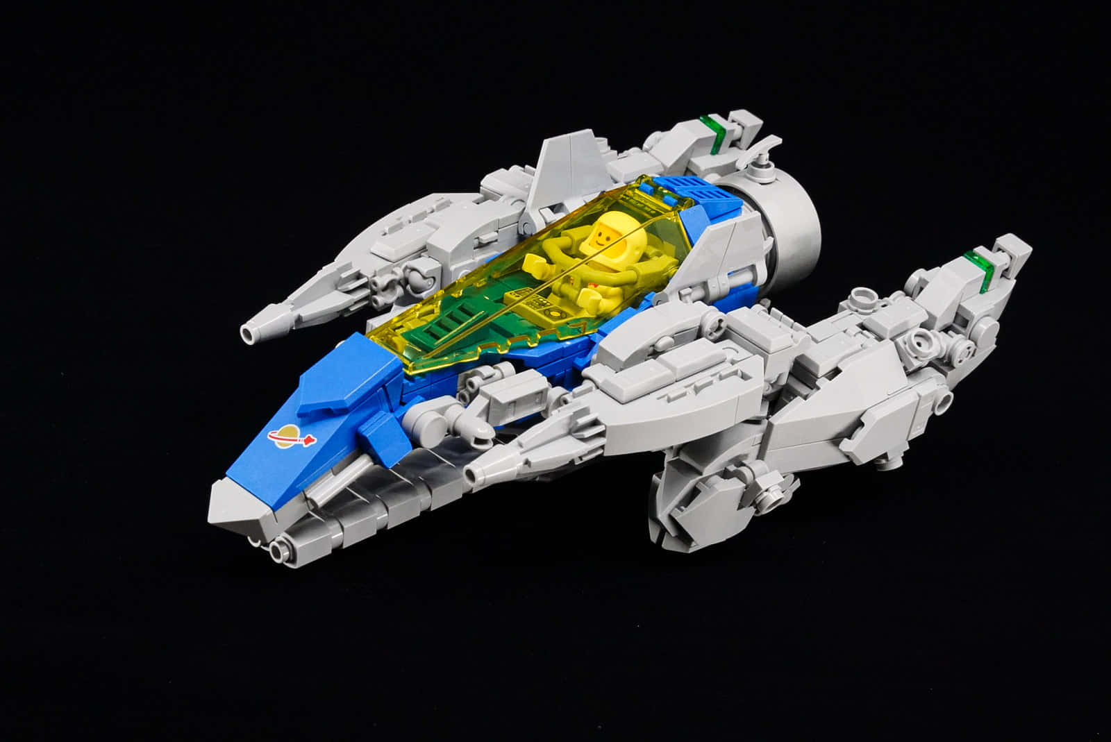 Spaceship 桌布 壁紙 — 一個詳細的LEGO太空船，帶有藍色和灰色面板，以及一個在透明駕駛艙內的黃色飛行員，背景為黑色。