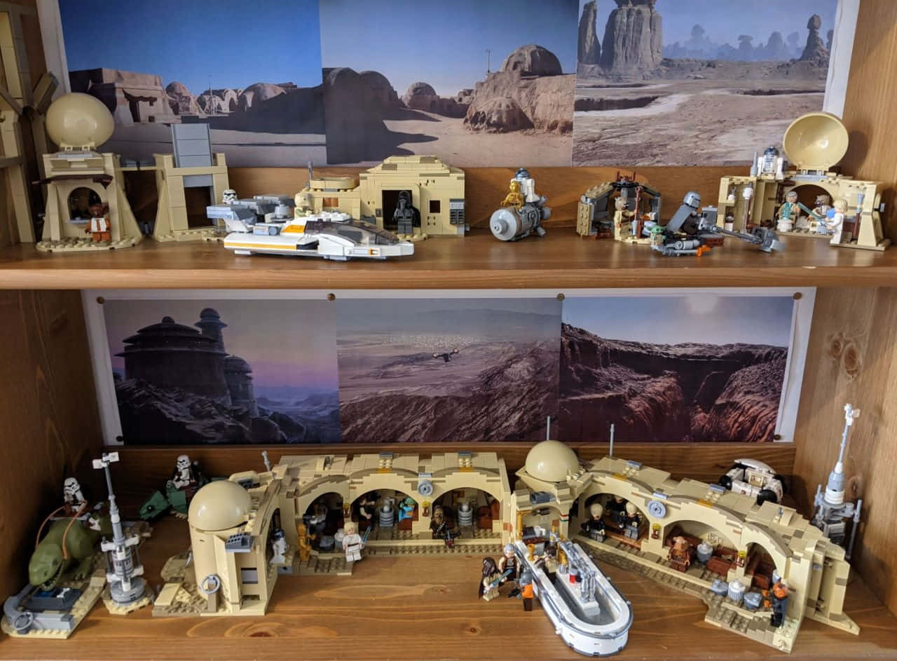 Tatooine 桌布 壁紙 — 一個詳細的LEGO星際大戰塔圖因立體模型，展示在木架上，配有沙漠背景海報的沙地爬行者和飛車模型。