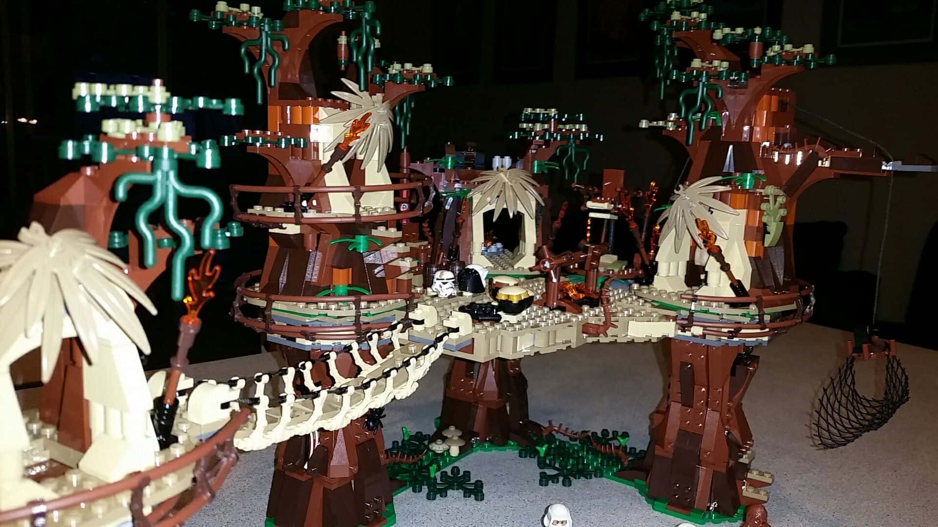 Ewok Village 桌布 壁紙 — 一個詳細的LEGO樹屋村莊，發光的綠色藤蔓和吊橋，背景為黑暗。