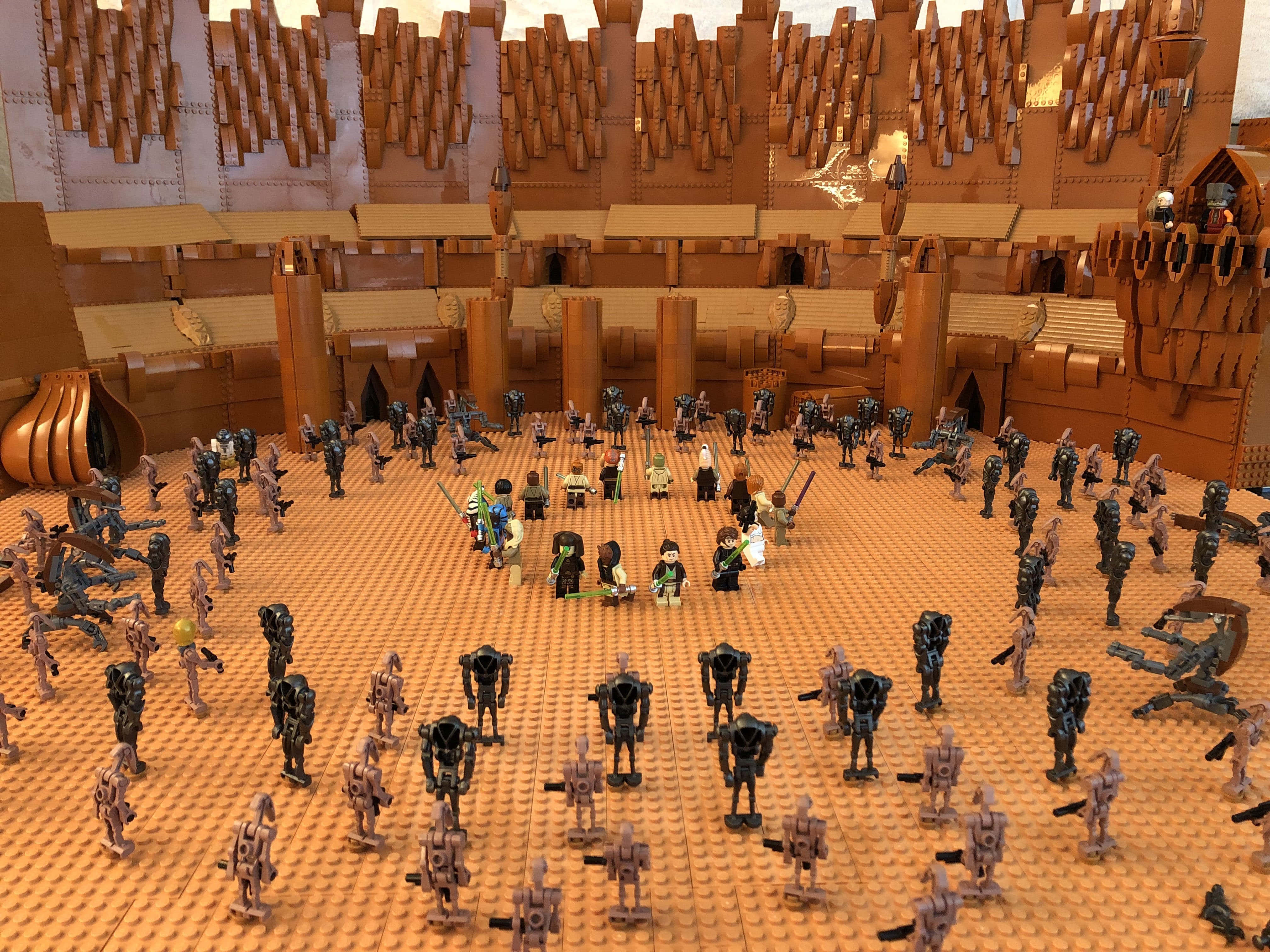 The Battle Of Geonosis 桌布 壁紙 — 一個詳細的LEGO立體模型描繪了一場大規模的戰鬥場景，在橙色底板上放置了眾多人偶和機器人，周圍環繞著複雜的棕色堡壘牆壁。