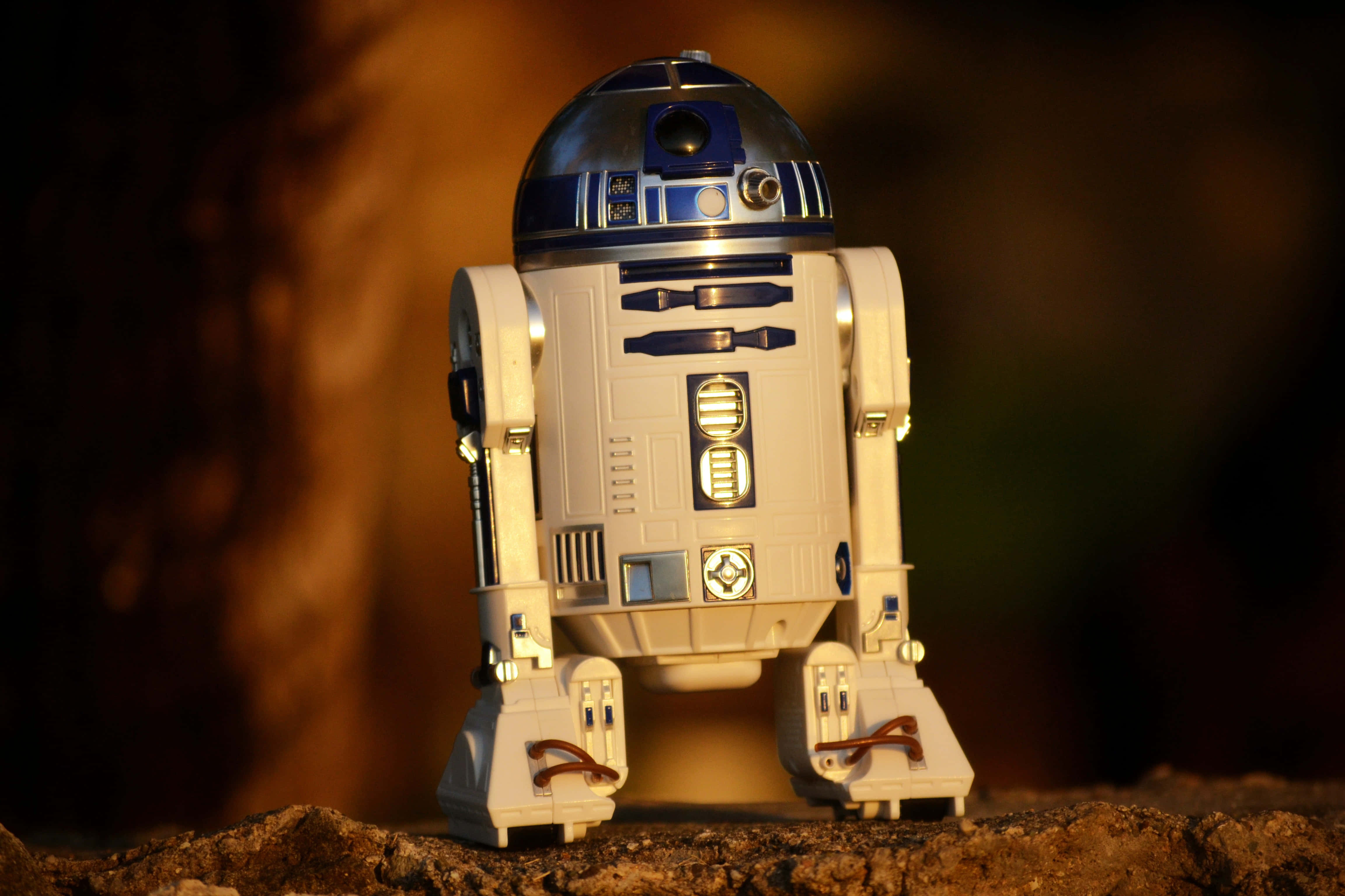 r2d2 桌布 壁紙 — 一個詳細的R2-D2機器人玩具站在岩石地形上，溫暖的金色燈光，背景模糊。