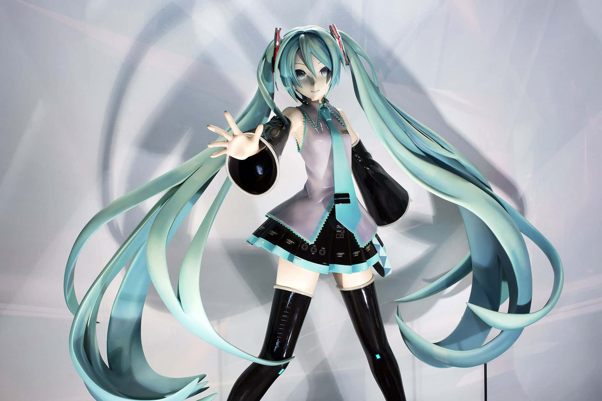初音未來 桌布 壁紙 — 一個詳細的初音未來動漫人偶，擁有長長的藍綠色雙馬尾和黑色服裝，在幾何灰色背景前動態擺姿勢。