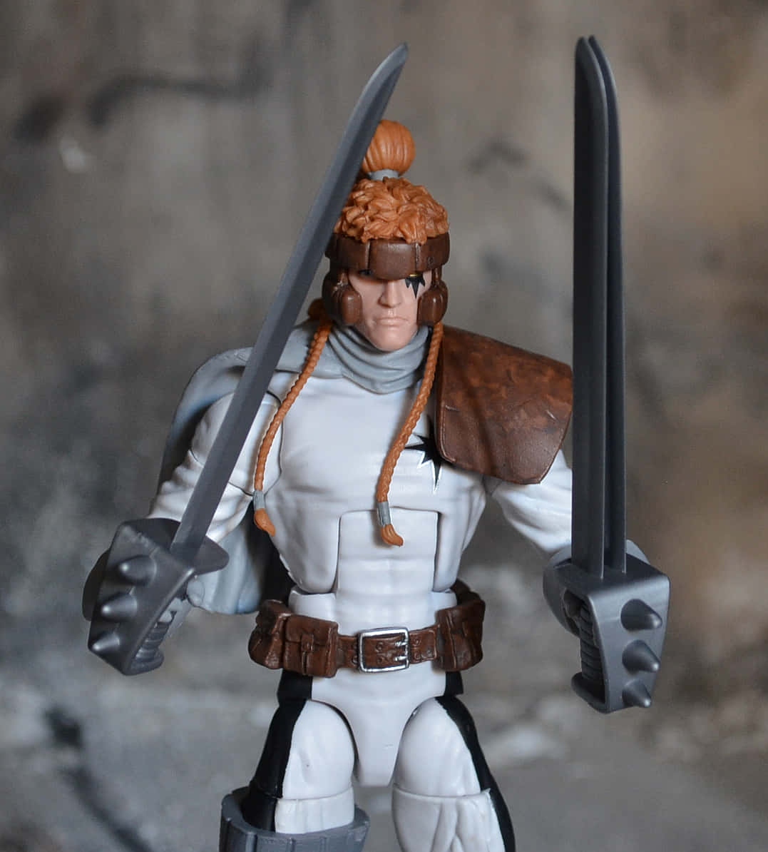 Shatterstar 桌布 壁紙 — 一個詳細的動作人偶，是一個有橙色辮子頭髮和兩把劍的戰士，站在模糊的石頭背景前。