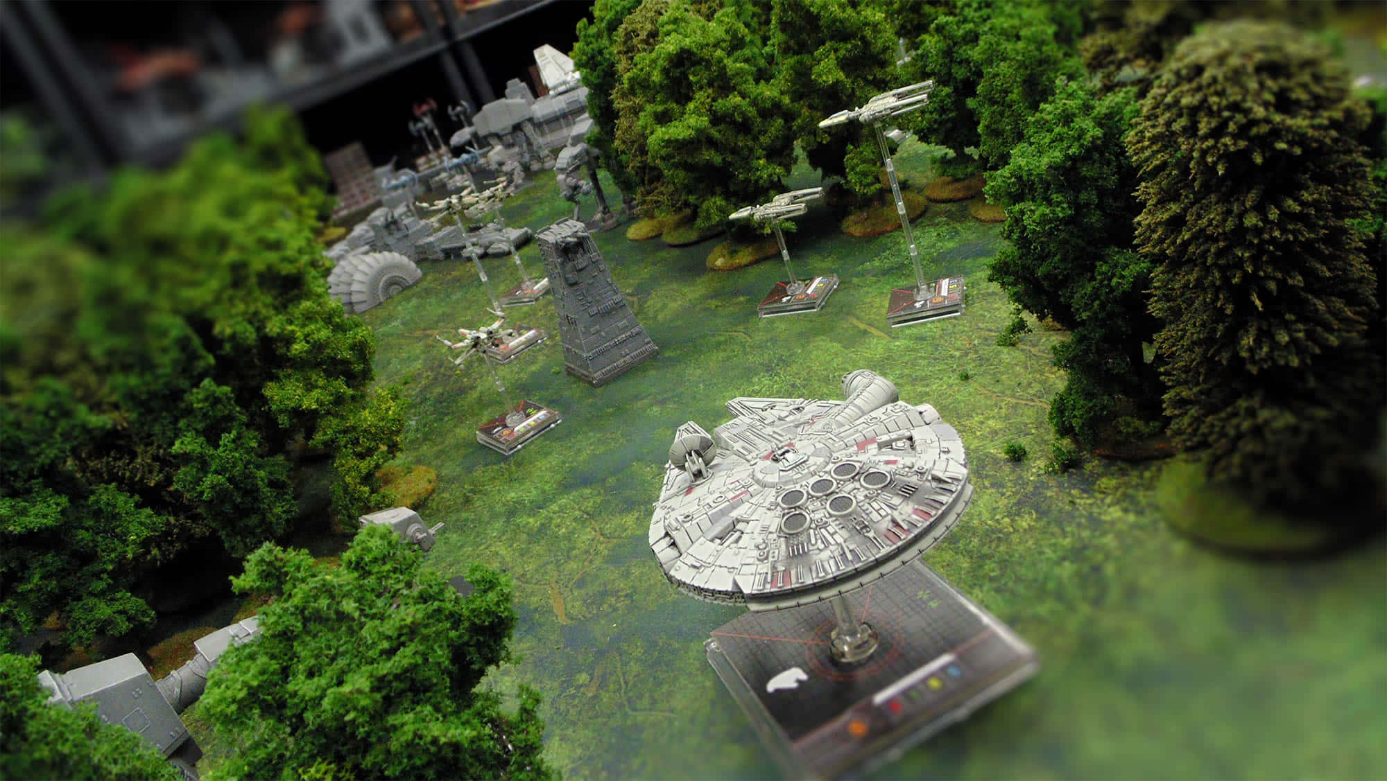 The Battle Of Endor 桌布 壁紙 — 一個詳細的千年鷹模型放置在茂密的綠樹和其他星戰微縮模型之間，位於森林立體模型戰場上。