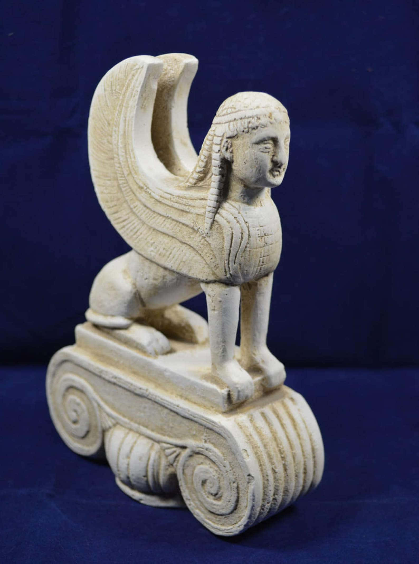 Mystical Artifacts 桌布 壁紙 — 一個詳細的奶油色獅身人面像雕塑，帶有翅膀和人頭，棲息在一個雕刻的輪式底座上，背景為深藍色。
