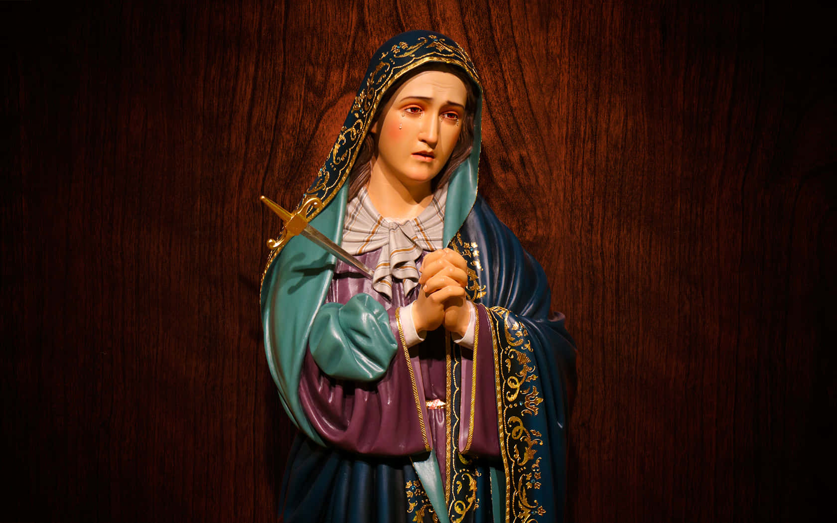 Catholic Desktop 桌布 壁紙 — 一個詳細的宗教人物雕像，身穿藍色和紫色長袍，在深色木質背景前手持劍。
