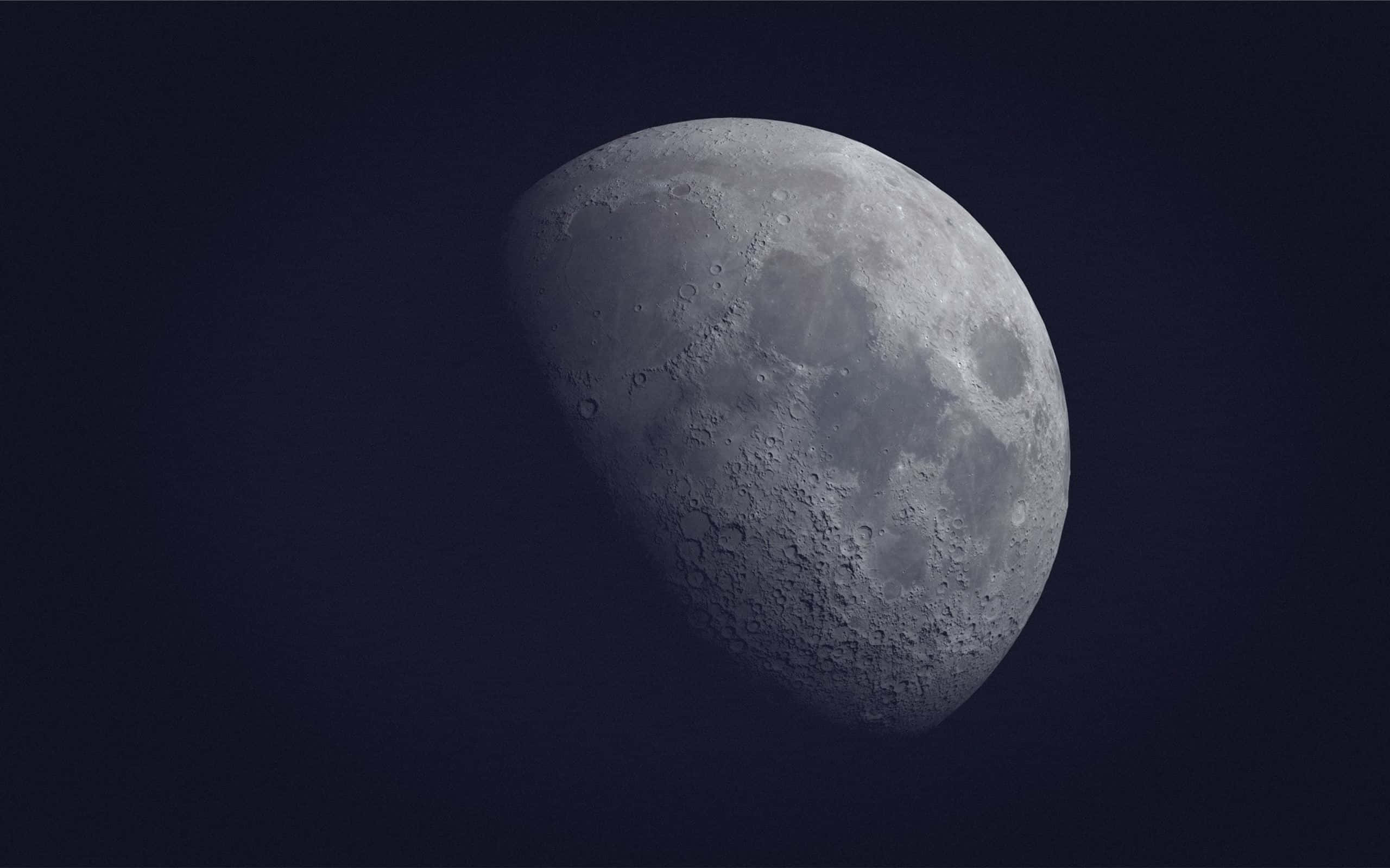 Cool Moon 桌布 壁紙 — 一個詳細的彎月，帶有隕石坑和月海，在深海軍藍色太空背景上柔和發光。