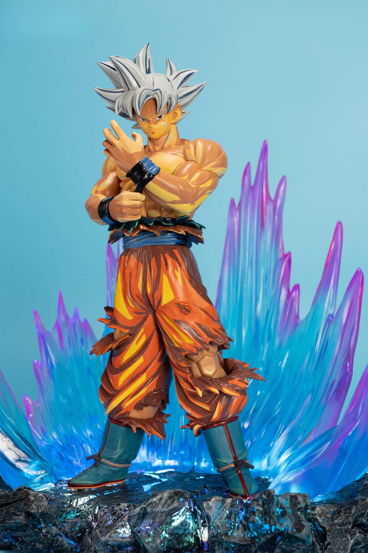 Mui Goku 桌布 壁紙 — 一個詳細的悟空超級賽亞人形態動漫人偶站在岩石地形上，身後有鮮豔的藍色和紫色水晶能量爆發。