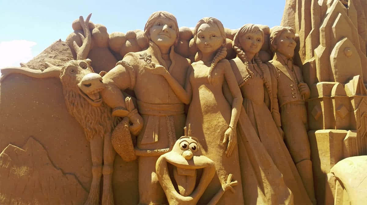 Sand Art 桌布 壁紙 — 一個詳細的沙雕描繪了《冰雪奇緣》中的角色，包括艾莎、安娜、奧拉夫和克里斯托夫，在清澈的藍天下。