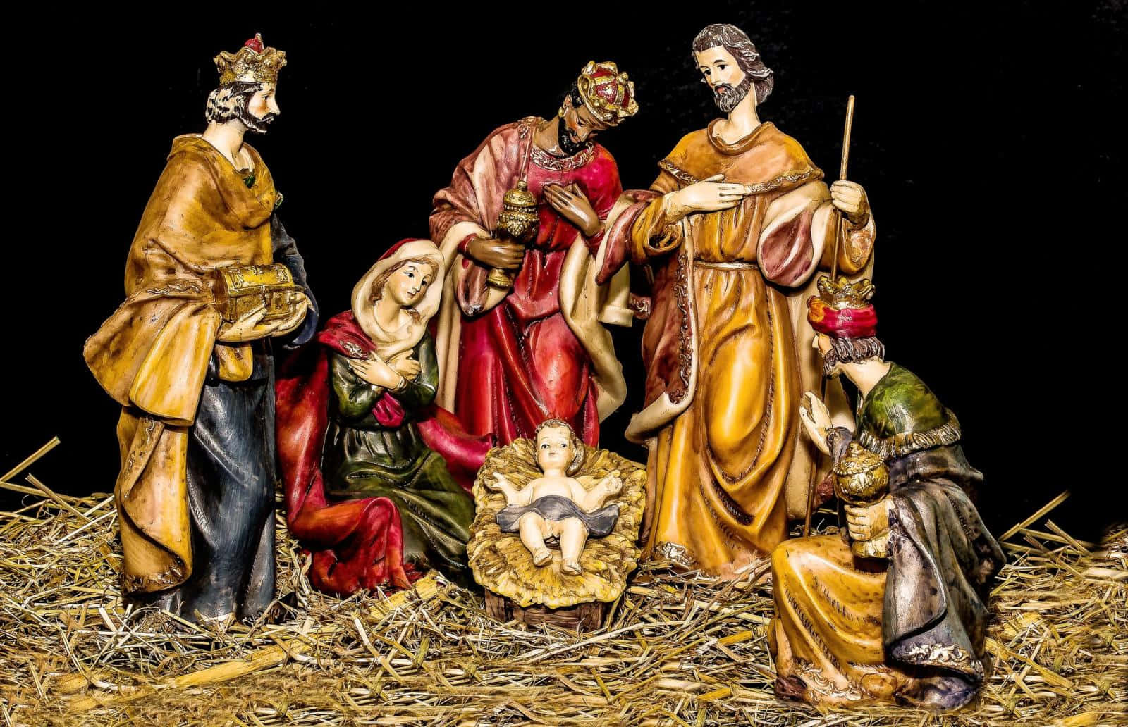 Nativity Scene 桌布 壁紙 — 一個詳細的耶穌誕生場景，人物穿著華麗長袍，聚集在黑色背景前稻草床上的馬槽裡的嬰兒周圍。