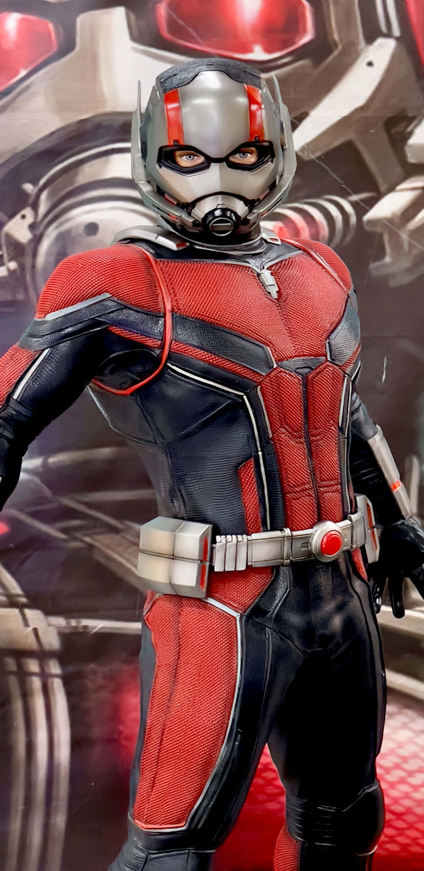 cosplay 桌布 壁紙 — 一個詳細的蟻人動作人偶，身穿紅黑戰衣，自信地站在未來機械背景前。