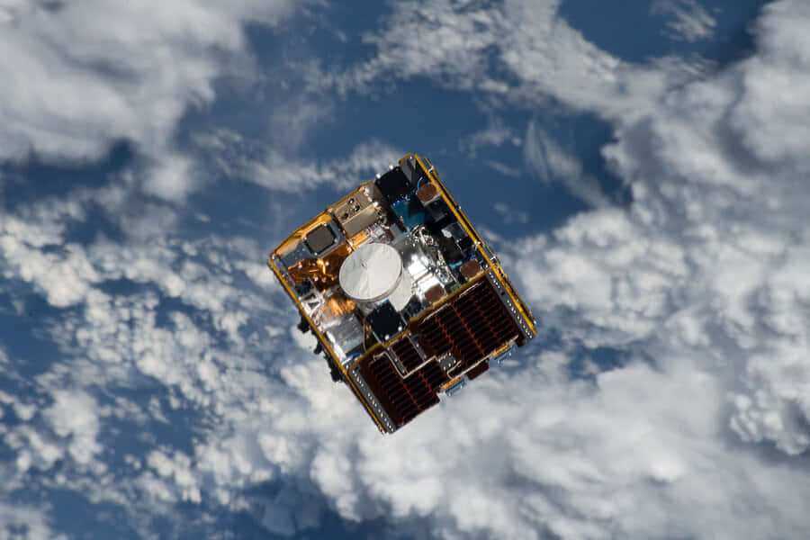 Space Debris 桌布 壁紙 — 一個詳細的衛星在地球藍白雲層覆蓋的表面上方軌道上漂浮。