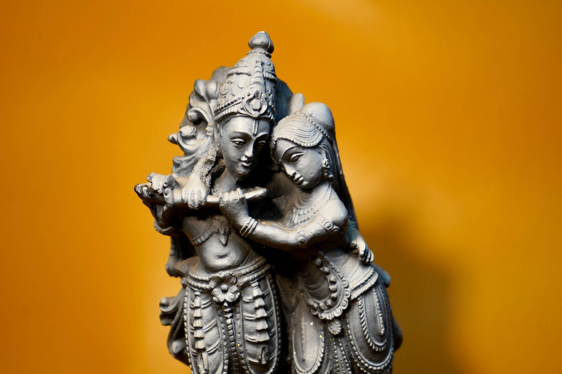 Hindu God 桌布 壁紙 — 一個詳細的銀色雕像，描繪一對神聖情侶在溫暖的橙色背景前擁抱。