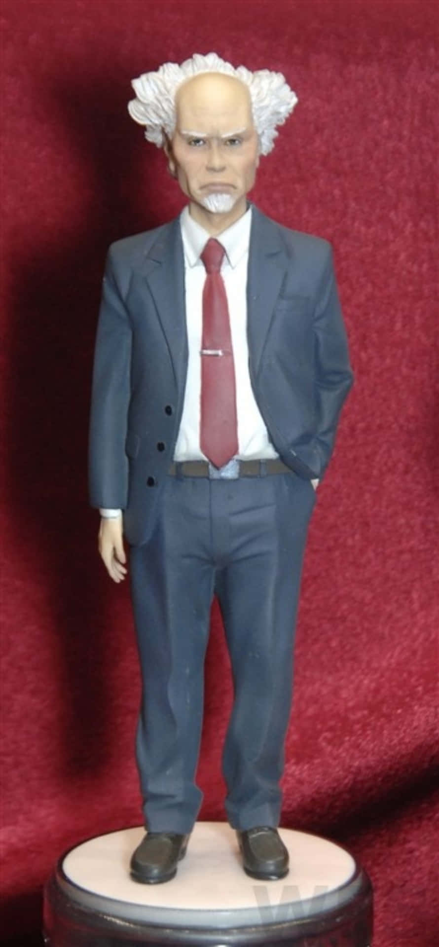 Ghost In The Shell Daisuke Aramaki 桌布 壁紙 — 一個詳細的雕像，一個嚴肅的男人，白髮和山羊鬍，穿著灰色西裝和紅色領帶，站在一個基座上，背景是深紅色天鵝絨。