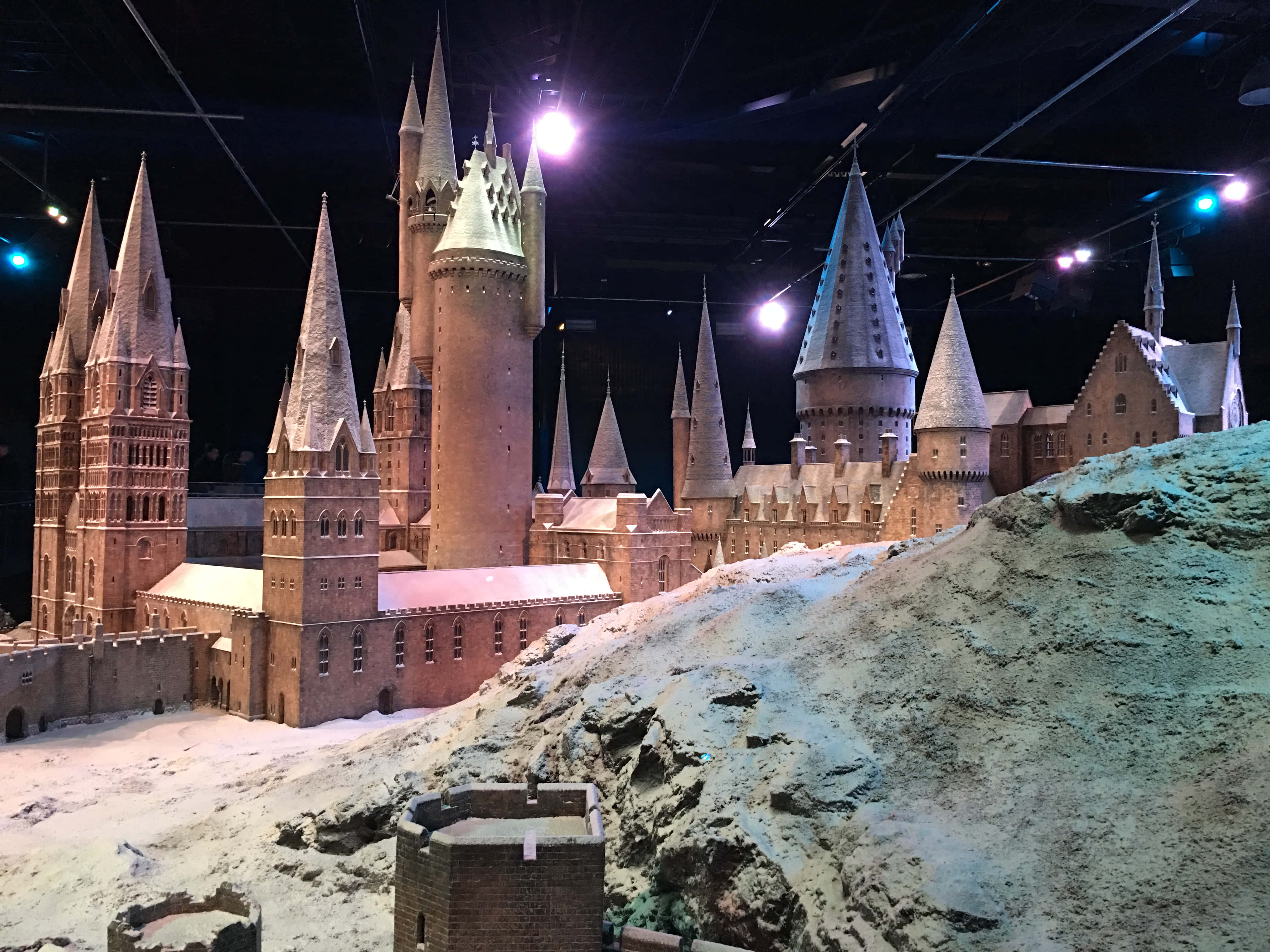 Hogwarts Castle 桌布 壁紙 — 一個詳細的霍格華茲城堡微型模型，在黑暗展覽天花板的背景下被聚光燈照亮。