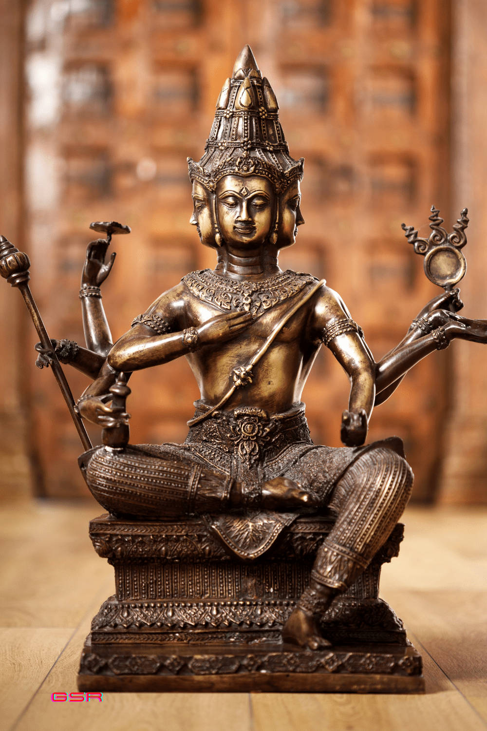 戴著冠冕的多臂神祇青銅雕像，坐在華麗的基座上。