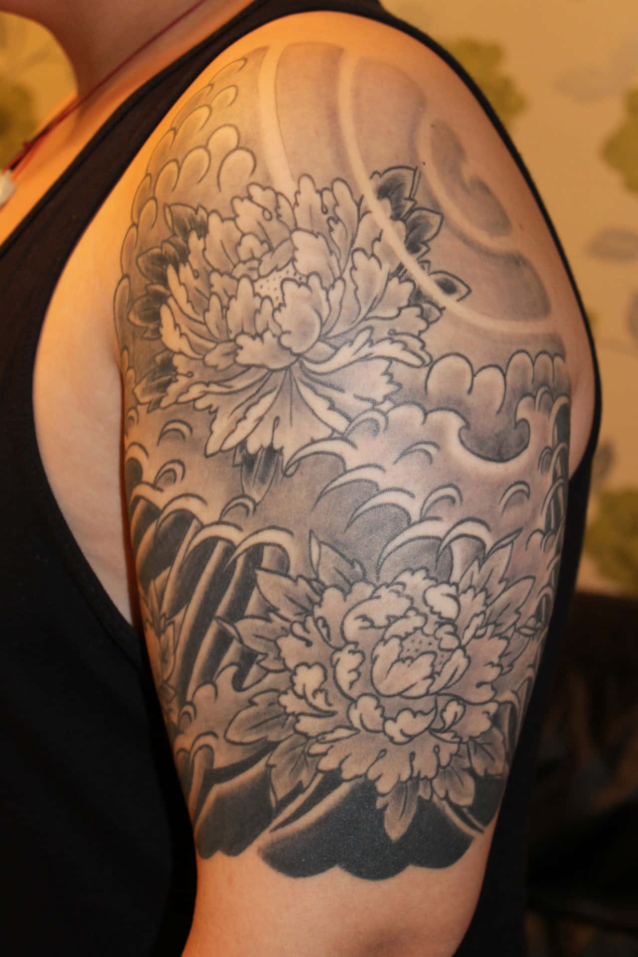 Tattoo 桌布 壁紙 — 一個詳細的黑灰刺青，描繪了兩朵被流動波浪環繞的大牡丹，覆蓋了一個人的肩膀和上臂。