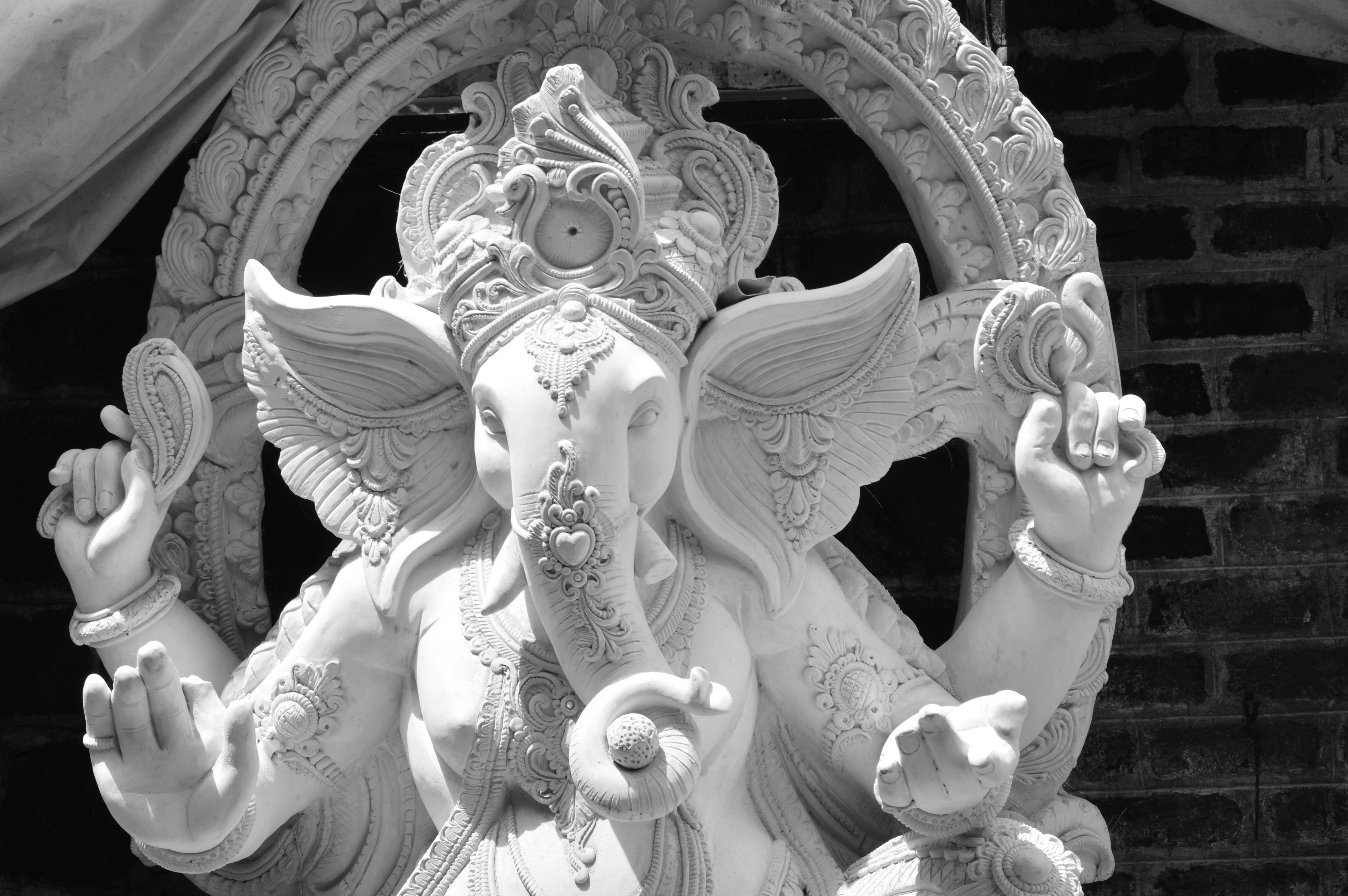 Bappa 桌布 壁紙 — 一個詳細的黑白象頭神雕像，擁有象頭和多臂，手持象徵物品，背景是磚牆。