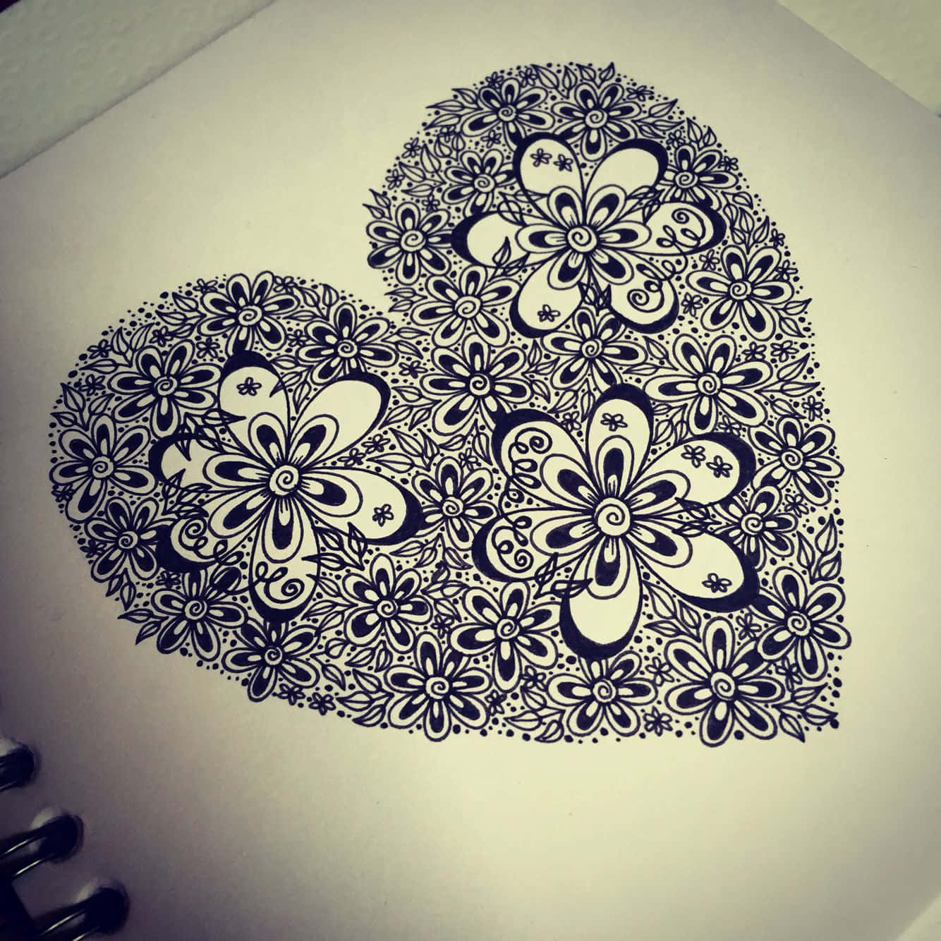 Heart Doodle 桌布 壁紙 — 一個詳細的黑色墨水心形，充滿複雜的花卉圖案，畫在螺旋筆記本頁面上。