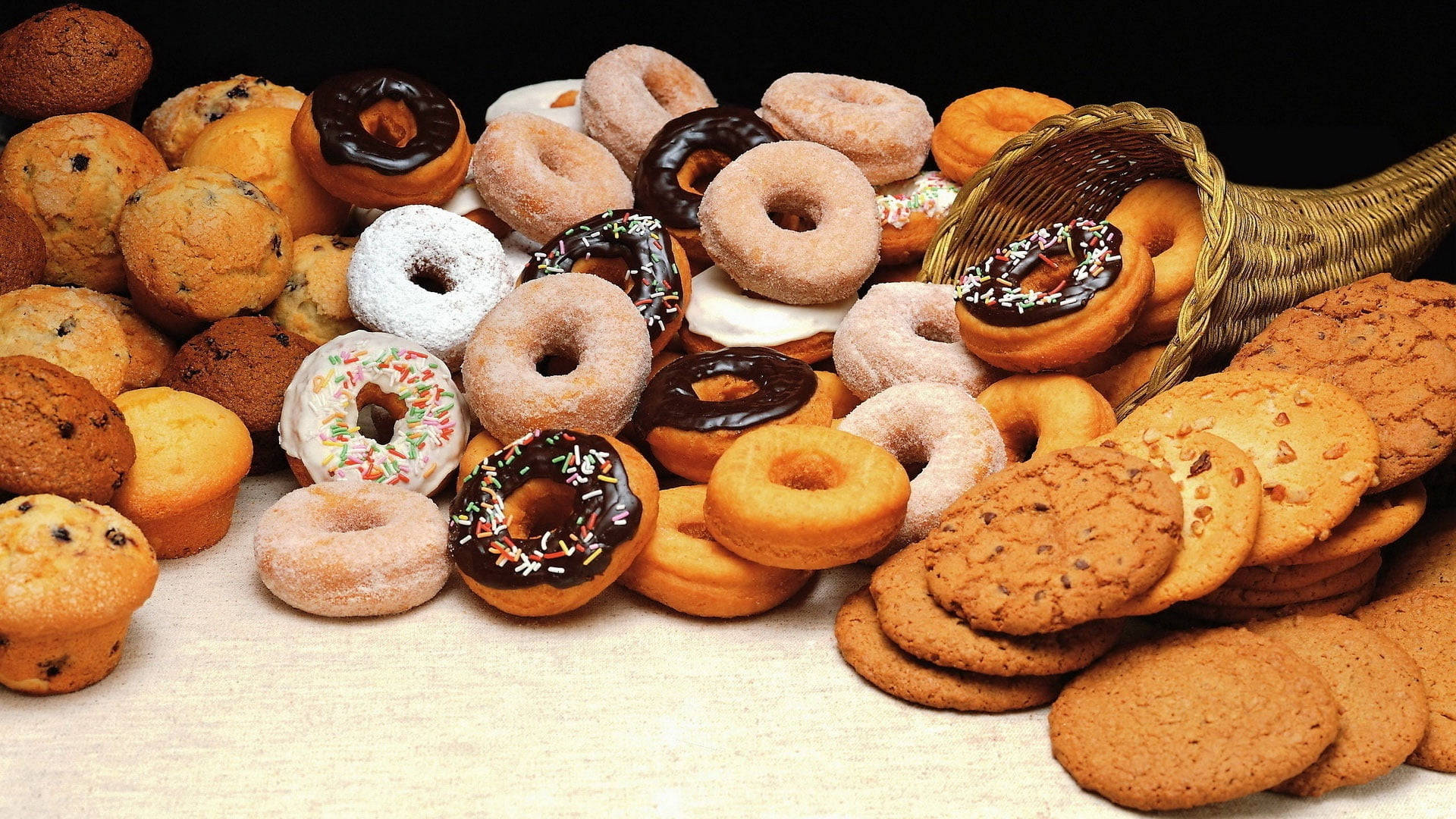Donut 桌布 壁紙 — 一個誘人的組合，包括釉面巧克力碎甜甜圈、鬆餅和巧克力餅乾，堆放在淺色木質表面上。
