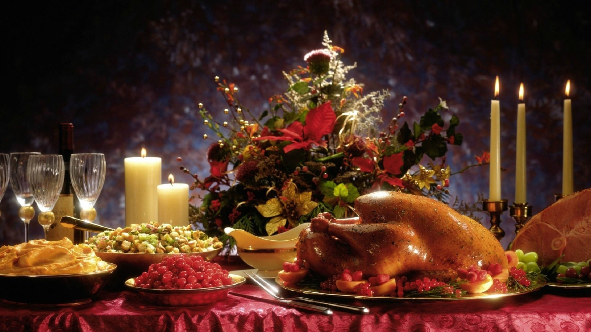 Thanksgiving Day 桌布 壁紙 — 一個豐富佈置的節日餐桌，有烤火雞、蔓越莓醬、蠟燭和節日花卉中心裝飾，在溫暖的燈光下。