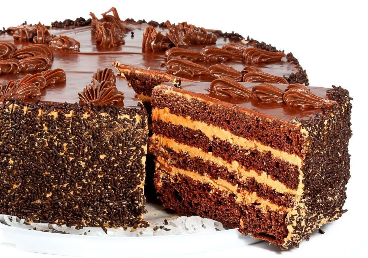 Chocolate Cake 桌布 壁紙 — 一個豐富的層疊巧克力蛋糕，帶有光澤的糖霜和彩針，切開一片後露出濕潤的蛋糕和奶油餡料。