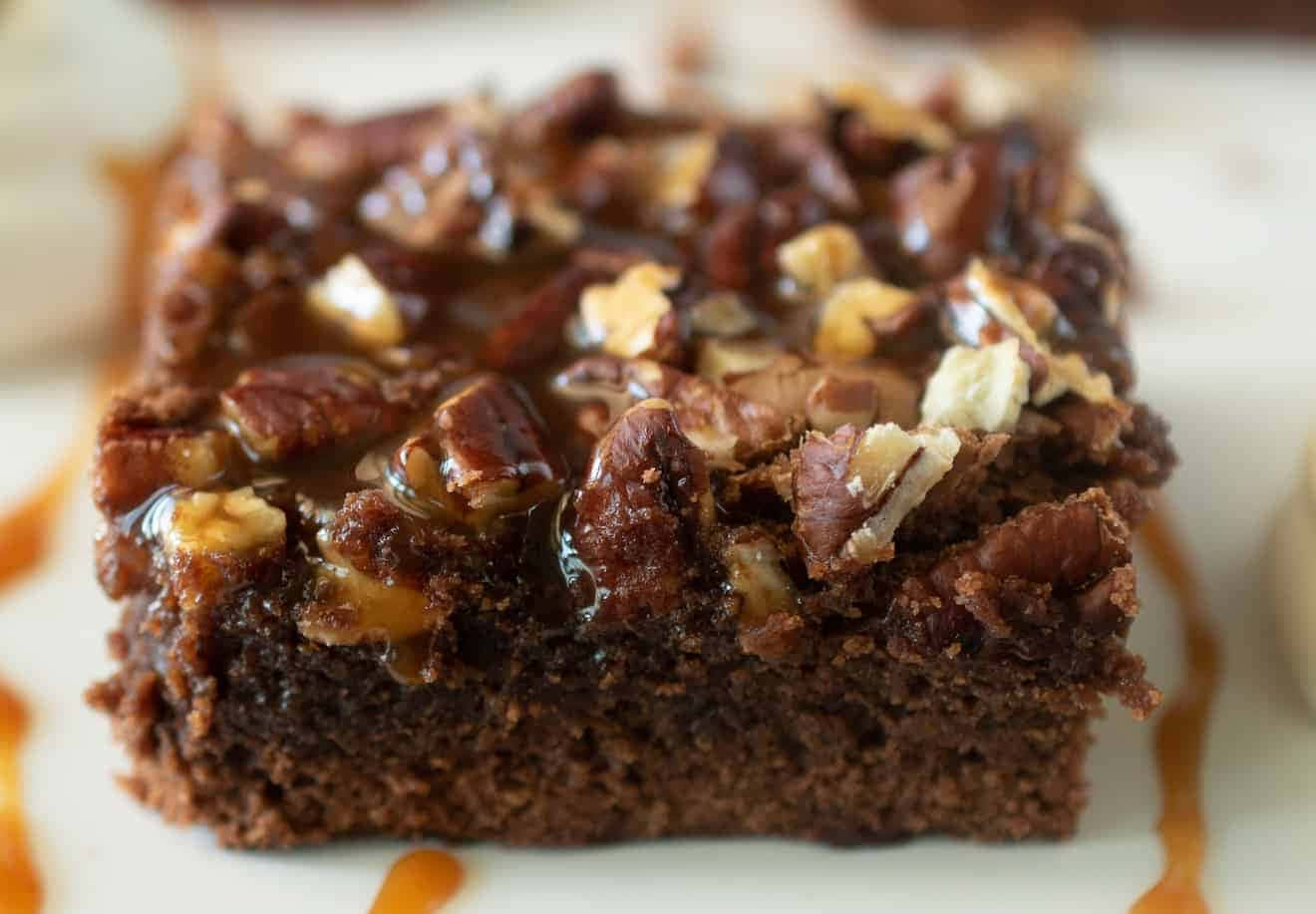 Caramel Brownie 桌布 壁紙 — 一個豐富的巧克力布朗尼，上面有光澤的焦糖和切碎的胡桃，放在白色盤子上。