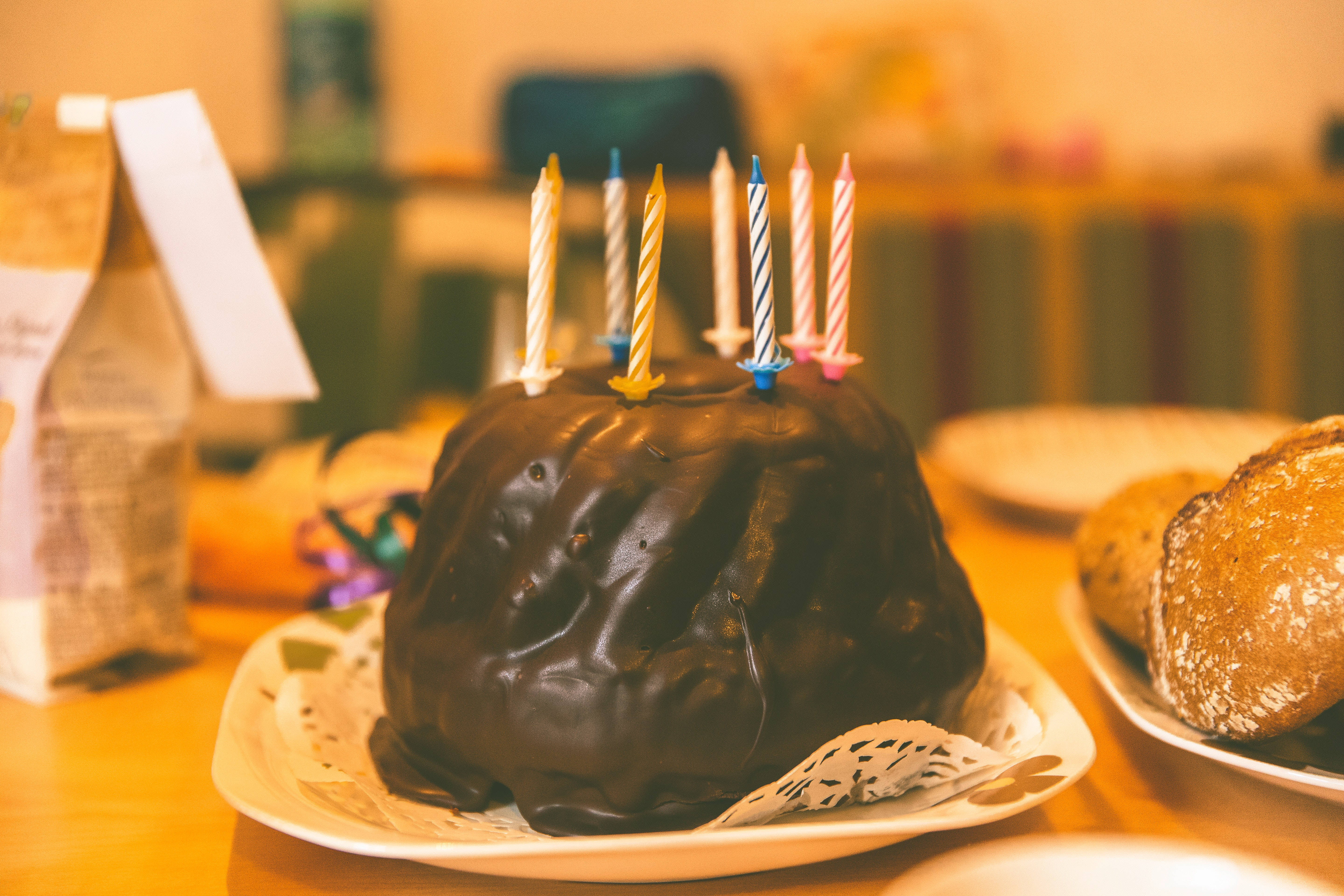 Birthday 桌布 壁紙 — 一個豐富的巧克力環形蛋糕，上面插著色彩繽紛的生日蠟燭，放在一個溫暖燈光的廚房裡的白色盤子上。