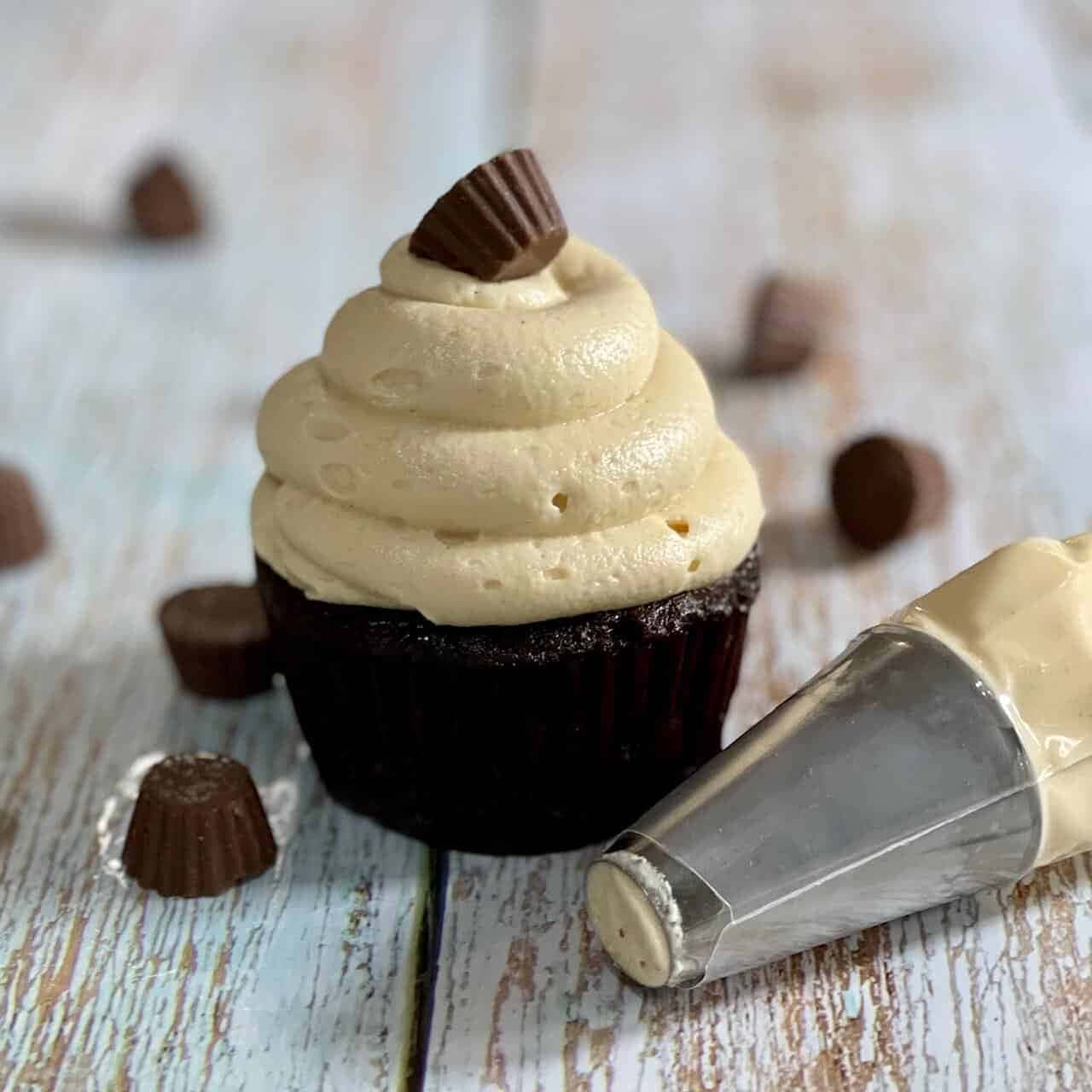 Buttercream 桌布 壁紙 — 一個豐富的巧克力紙杯蛋糕，上面有奶油花生醬糖霜和一個Reese's花生醬杯，旁邊有一個裱花袋，放在質樸的木質表面上。